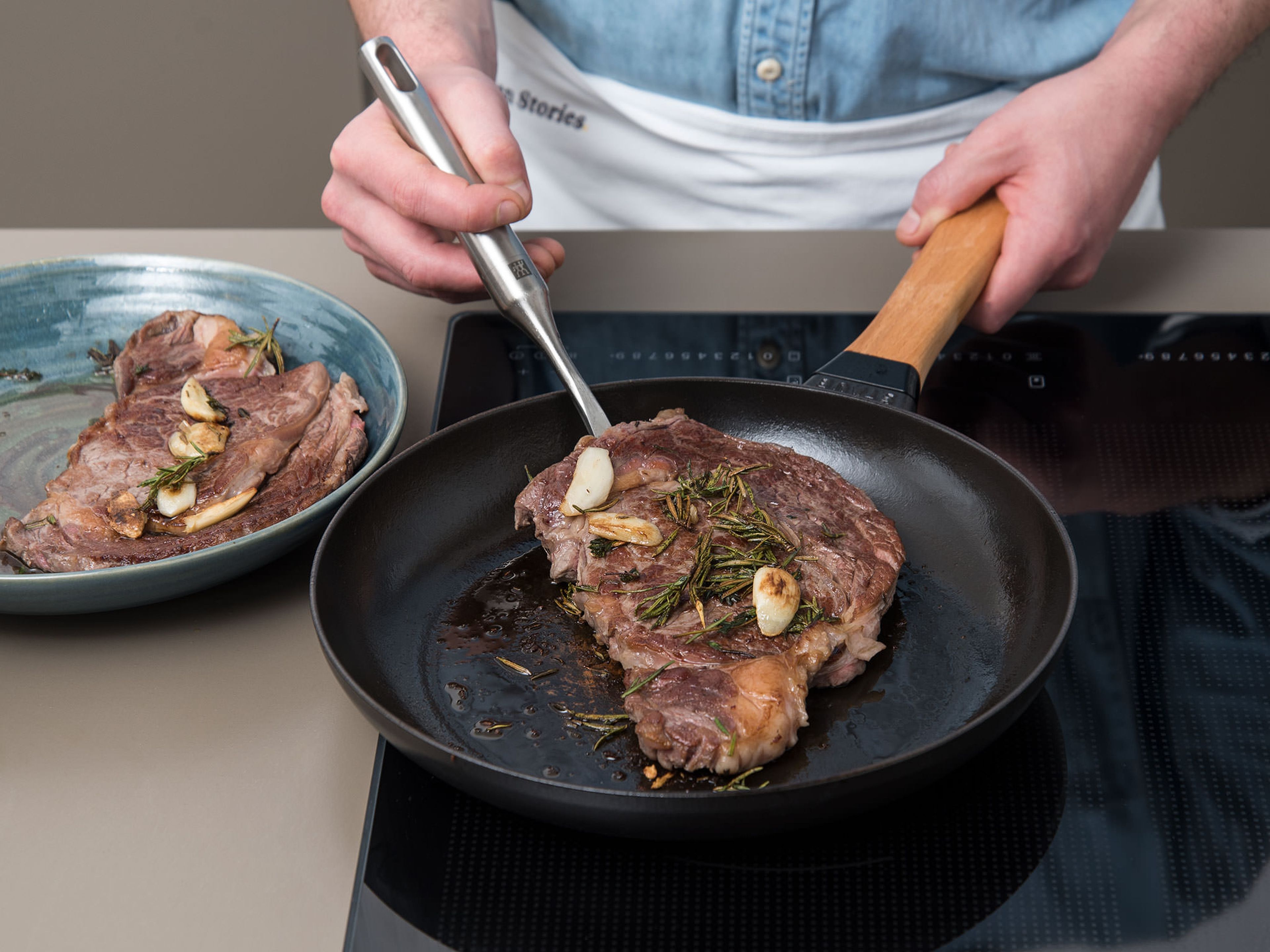 Währenddessen den Backofen auf 60°C vorheizen. Eine gusseiserne Pfanne auf mittlerer bis hoher Stufe erhitzen. Sobald die Pfanne vollständig erhitzt ist, Steaks aus dem Gefrierbeutel nehmen, mit Kräutern und Knoblauch in die Pfanne geben und von beiden Seiten ca. 4 – 5 Min. scharf anbraten. Steaks mit Kräutern und Knoblauch auf einen tiefen Teller geben. Mit einem flachen Teller bedecken und im Ofen bei 60°C ca. 8 – 10 Min. ruhen lassen.