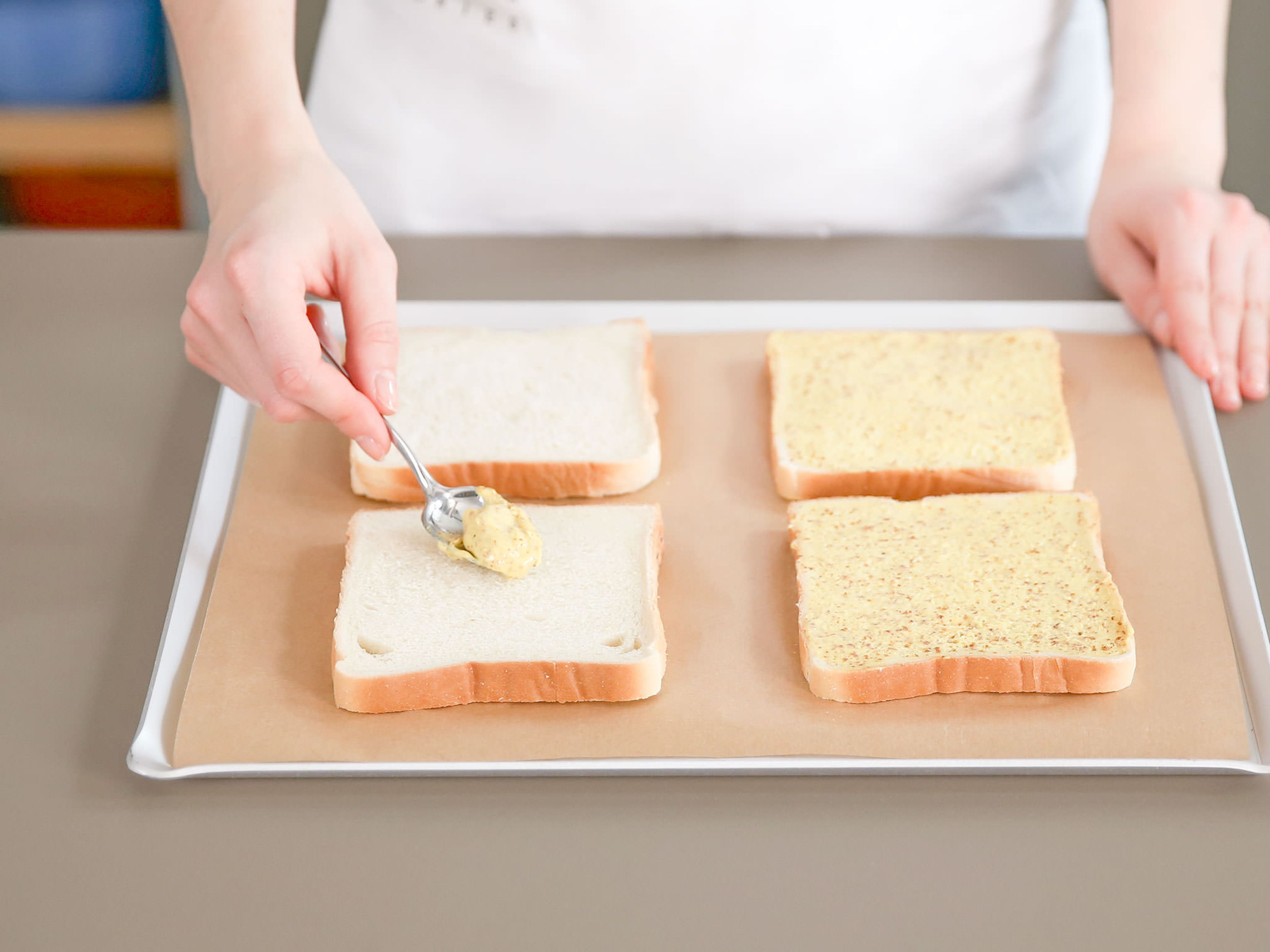 Preheat oven to 200°C/390°F. Place half of toasts on a parchment-lined baking sheet.Spread an even layer of mustard over them . Follow up with a slice of ham, a slice of cheese, and an even layer of part of the sauce Mornay.