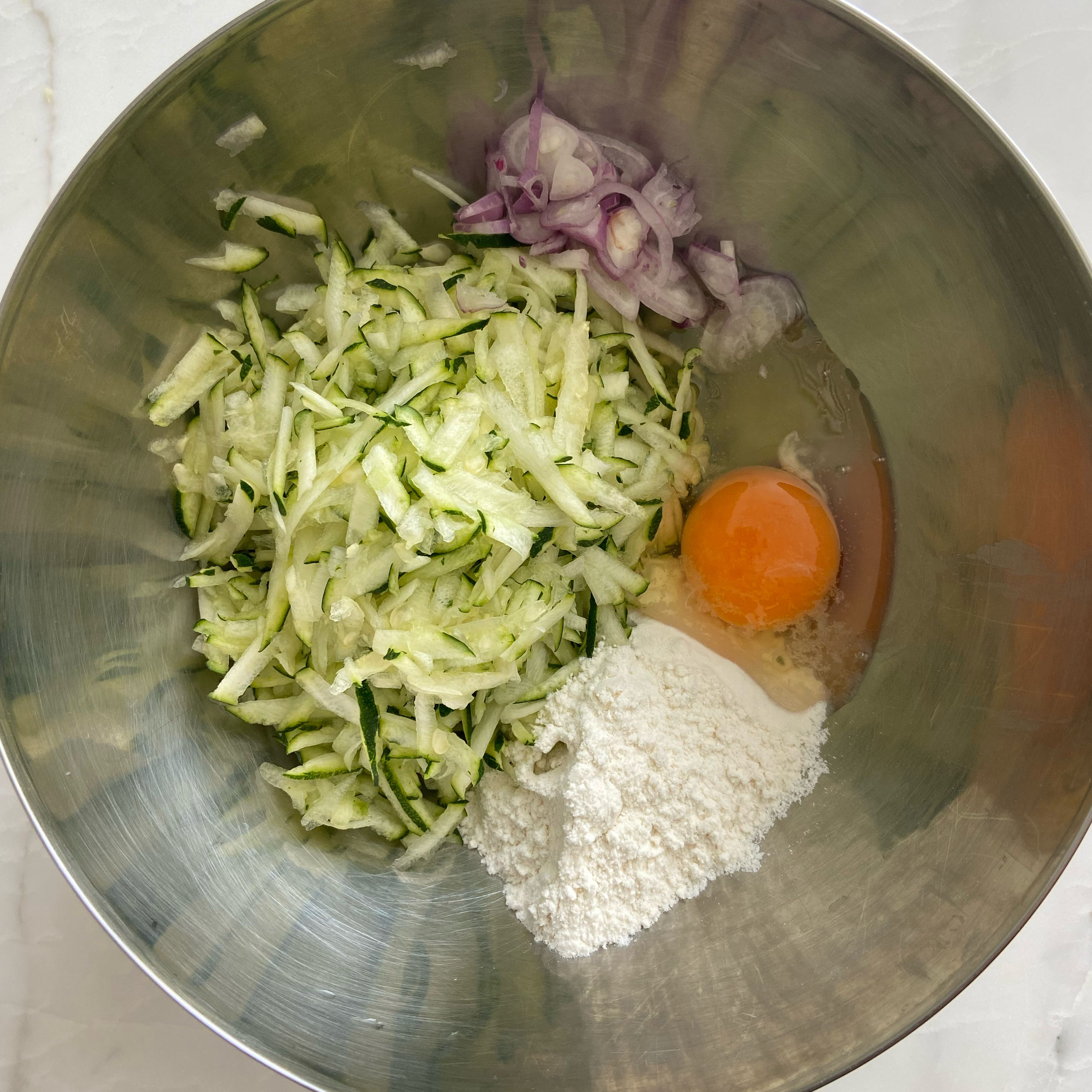 In a large mixing bowl, Add grated zucchini, flour, egg, onions and season with salt and black pepper