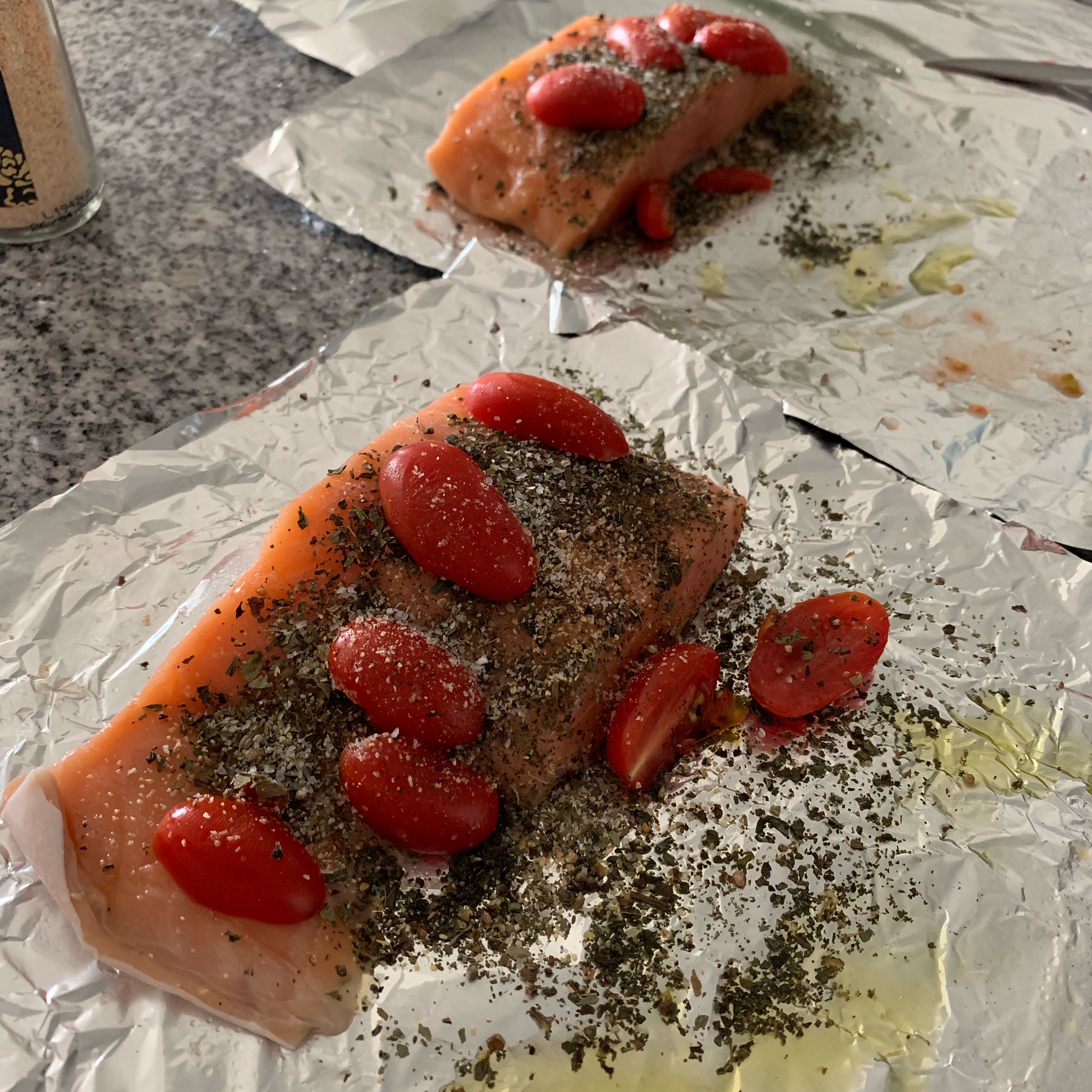 For each, place one 12—inch-Iong sheet of aluminum foil on top of another. Smear top sheet with 1/2 tablespoon olive oil, and layer a fillet of salmon, 6 tomato halves, salt and pepper, 4 basil leaves and another half tablespoon oil. Add garlic powder on both fillets. Add pepper and salt to taste. Seal package (I like to seal them with skin looking up, to avoid the skin to adhere into the aluminum).