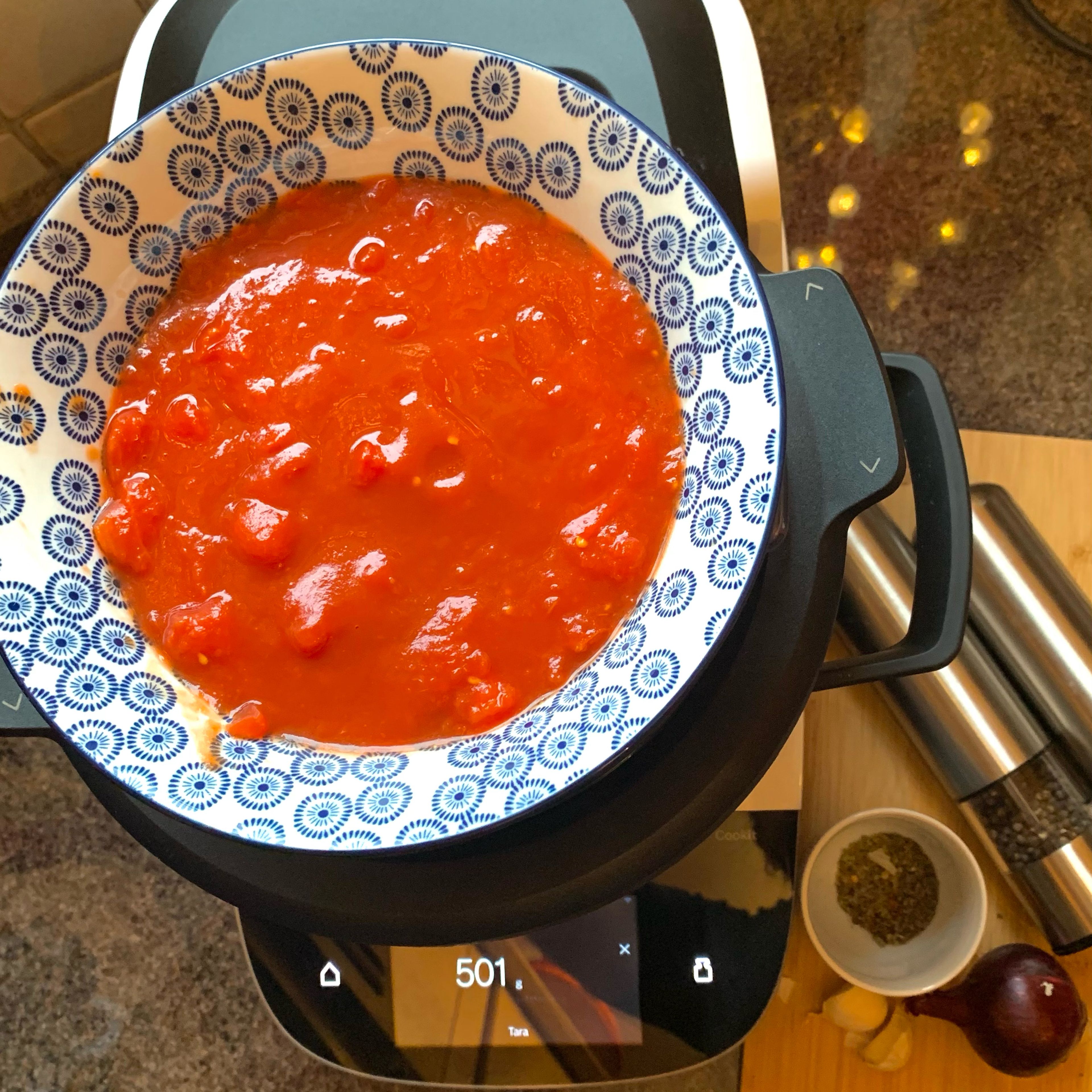 Die Pizza-Tomaten in einer Schüssel abwiegen und zu den Zwiebeln im Topf hinzufügen. Den Messbecher einsetzen, Oregano, Basilikum, Chilli sowie Salz und Pfeffer hinzugeben und nun alles köcheln lassen (Universalmesser| Stufe 5 | 98 C | 5 Min.).