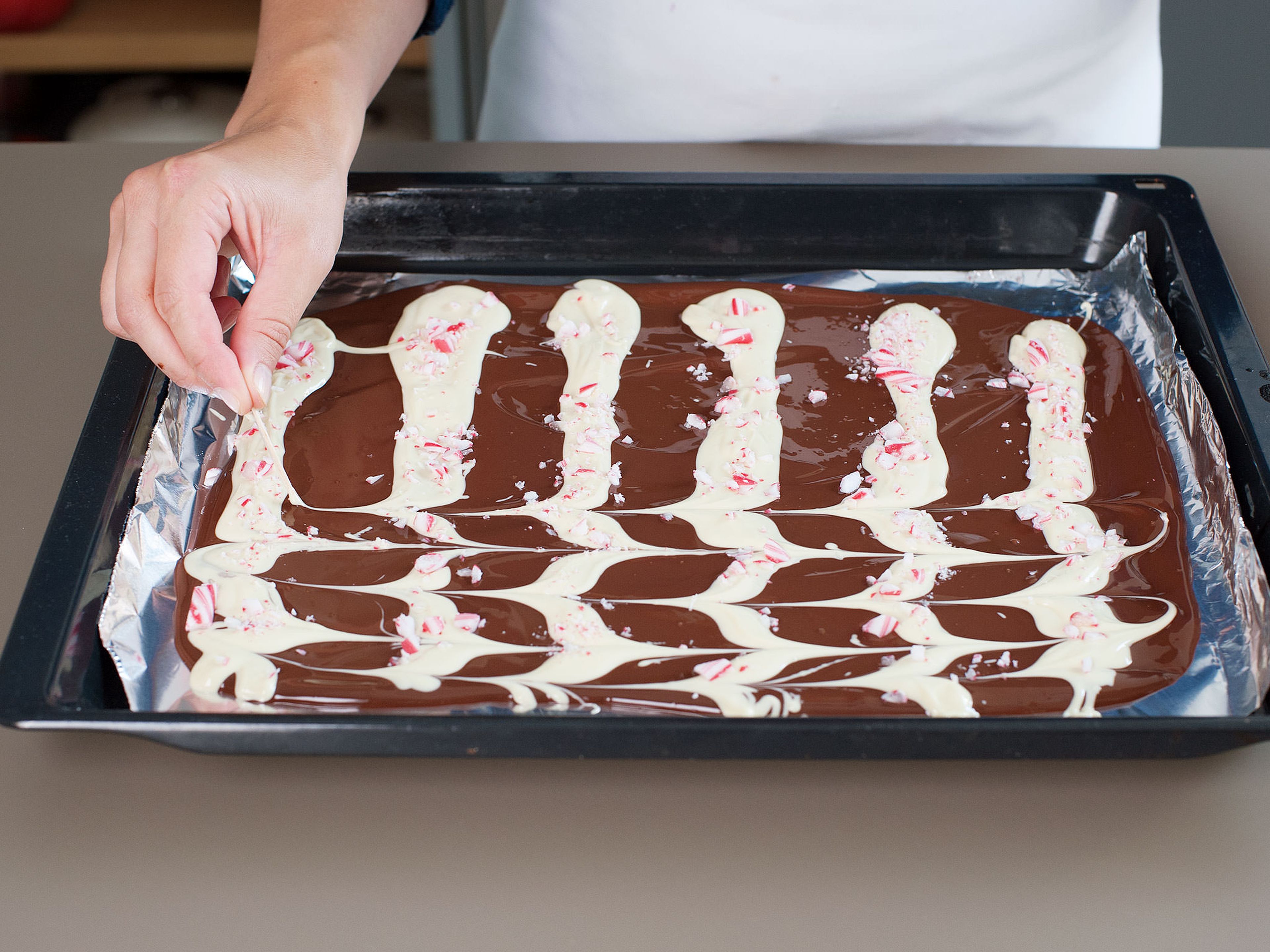 Sprinkle the crushed candy canes over white chocolate stripes. Drag a toothpick perpendicularly through the white chocolate to create the swirl. Place baking sheet on a level surface in refrigerator to harden for approx. 45 min. Cut or break into squares and serve. Store refrigerated in an airtight container.