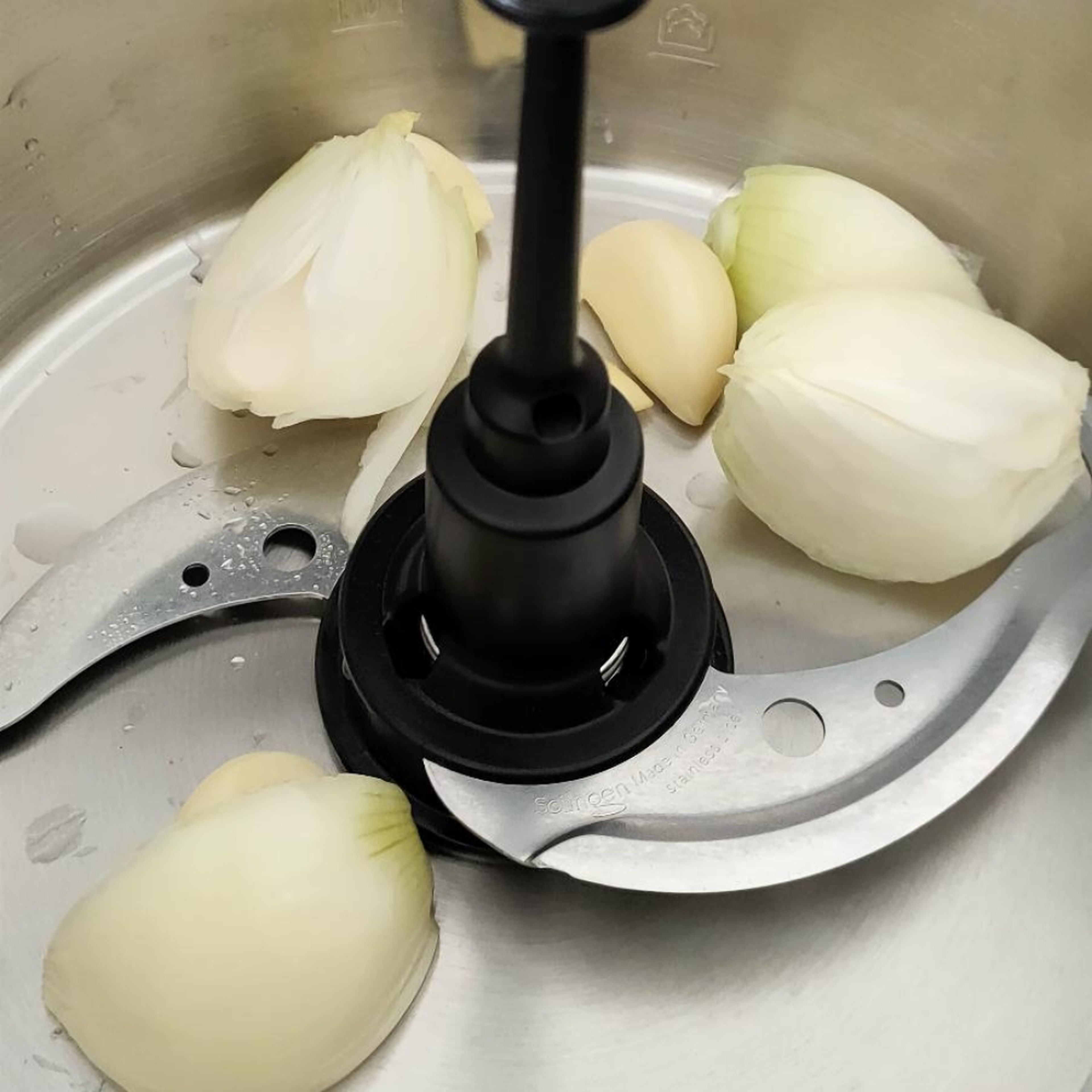 Universalmesser einsetzen. Zwiebel und Knoblauch schälen. Zwiebel vierteln. Beides in den Topf geben und bei geschlossenem Deckel und eingesetztem Messbecher zerkleinern (Universalmesser | Stufe 14 | 10 Sek.).