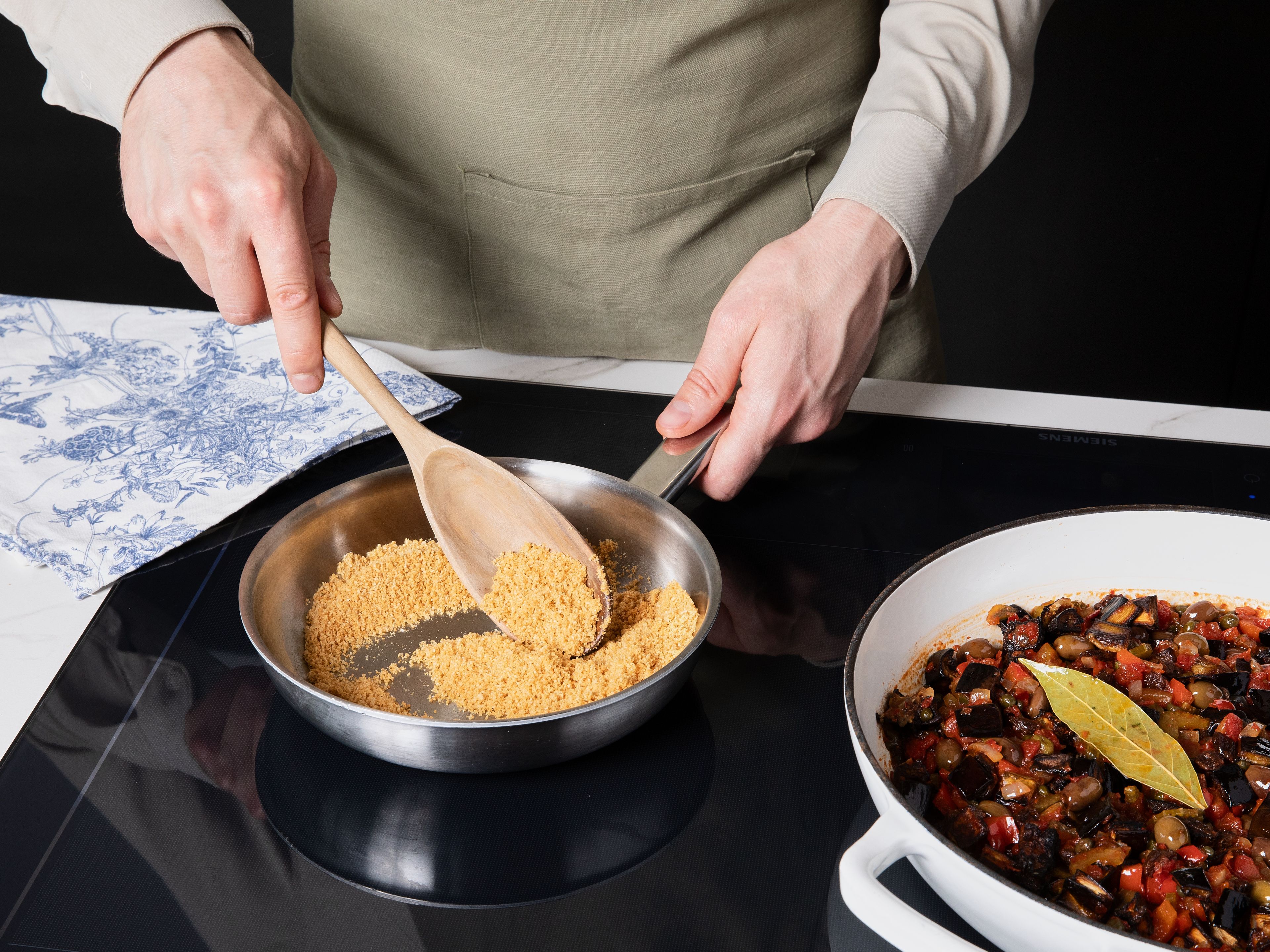 Die gerösteten Auberginen zur Sauce geben und vorsichtig unterheben. Nochmals abschmecken, dann vom Herd nehmen und ziehen lassen. Für das Topping frisch geriebenen Parmesan mit Semmelbröseln vermengen. In einer Pfanne ohne Öl bei mittlerer Hitze rösten, bis die Mischung goldbraun und knusprig ist.