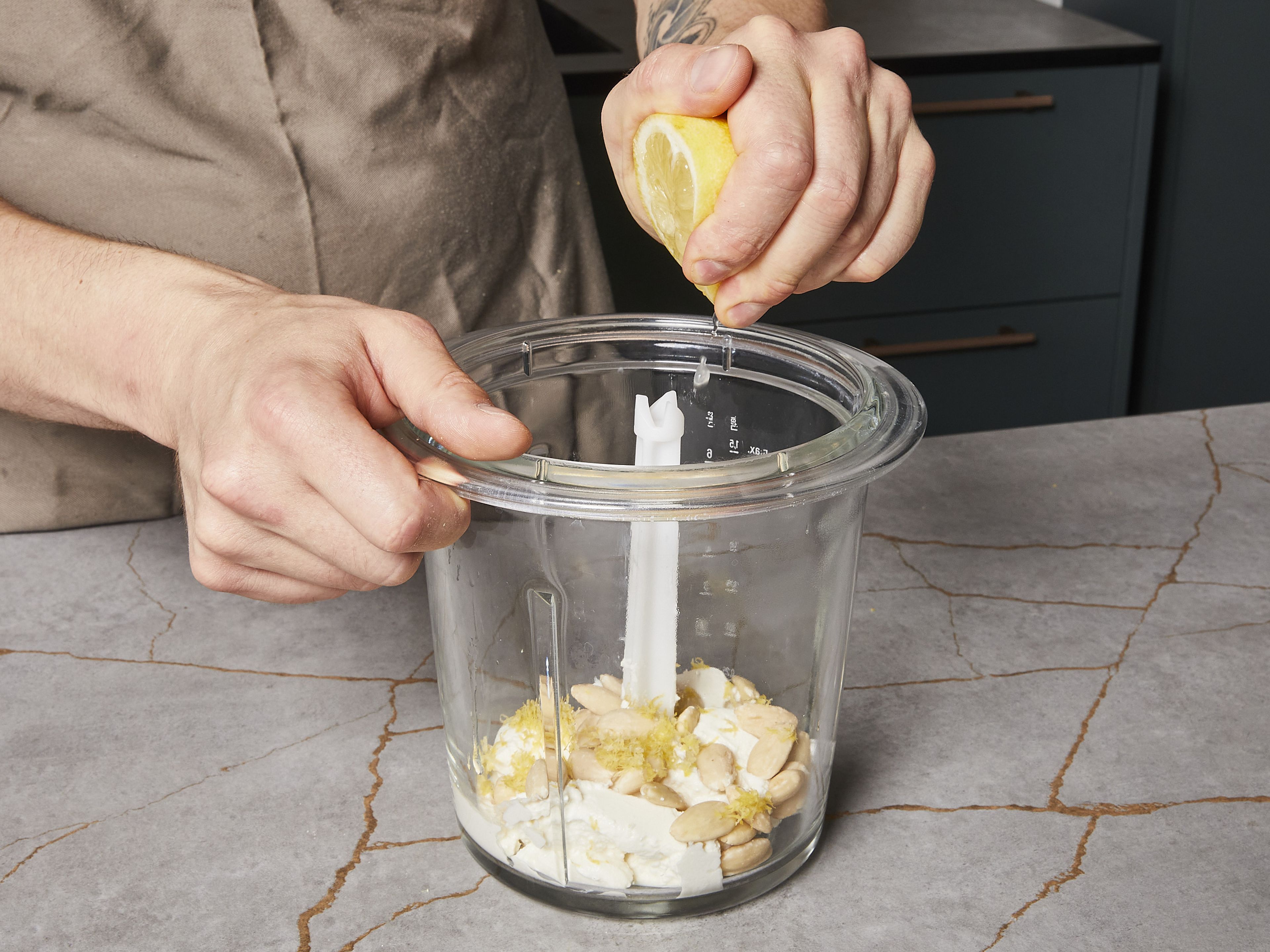 In der Zwischenzeit den Basilikum-Ricotta-Dip zubereiten. Dafür Basilikum fein hacken sowie Ricotta und Mandeln in einen Mixer geben. 1 TL Zitronenschale abreiben und dazugeben. Die Zitrone halbieren und den Saft auspressen, dann zur Ricotta-Mischung geben. Alles in einem Standmixer oder mit einem Stabmixer pürieren. Gehackten Basilikum und das restliche Olivenöl untermischen. Mit Salz und Pfeffer abschmecken und beiseitestellen.
