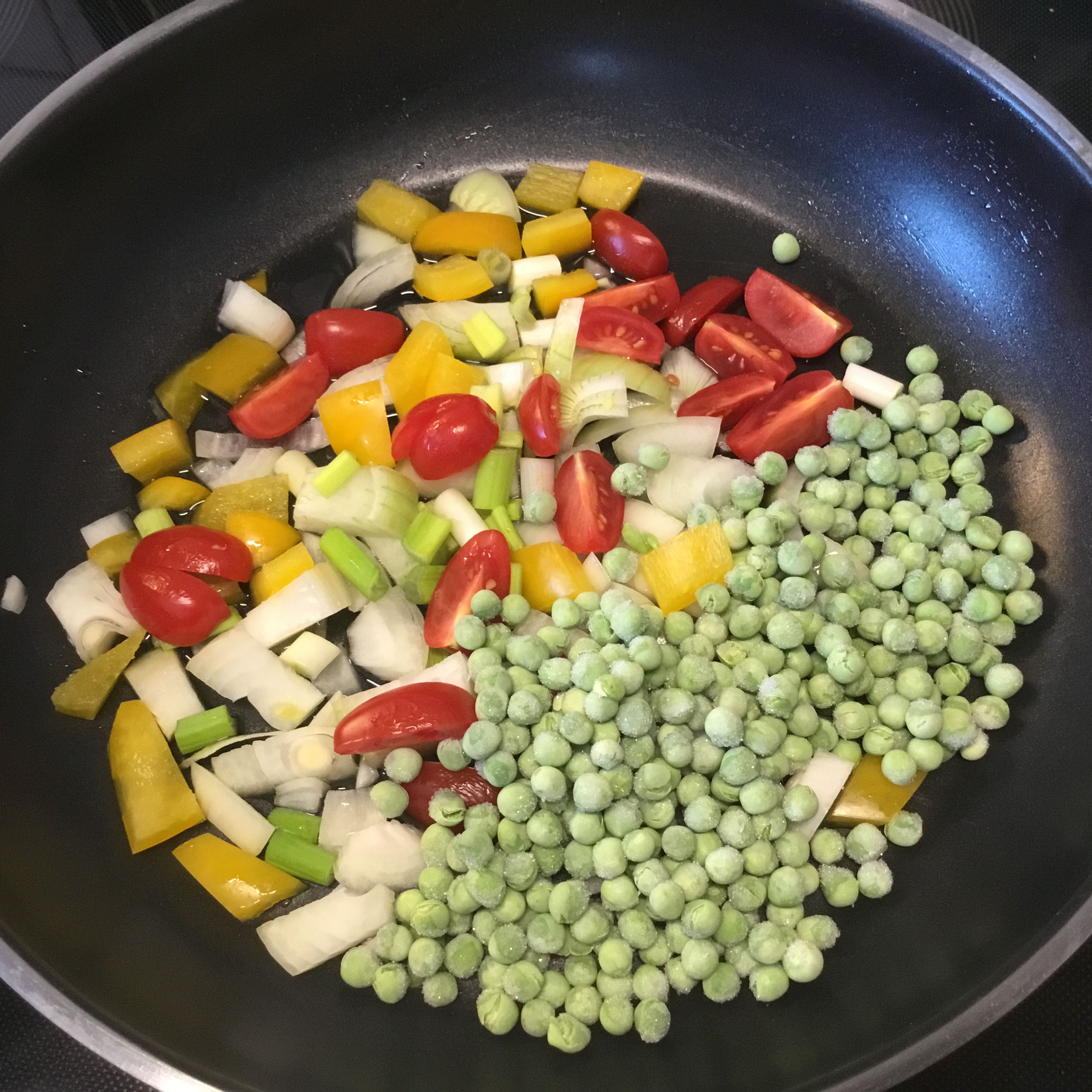 Die Zwiebeln, 1/4 Paprika, Kirschtomaten, Frühlingszwiebeln putzen und in kleine Teile schneiden. Die Erbsen hinzufügen. Das Gemüse in wenig Öl ein mit niedriger Temperatur anbraten.