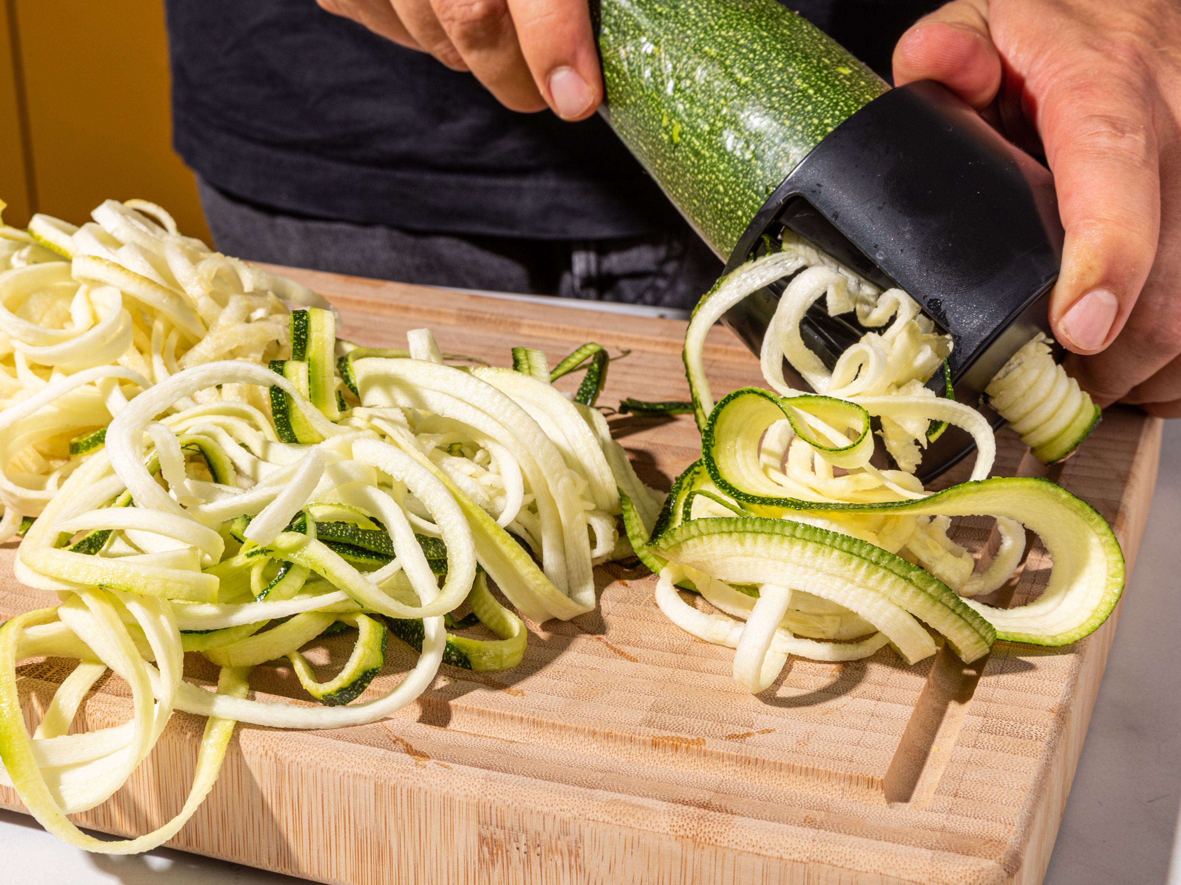 Zucchinis mit einem Spiralschneider in mitteldicke Spiralen schneiden. Direkt auf zwei Teller aufteilen und beiseitestellen. Knoblauch und Schalotte schälen.