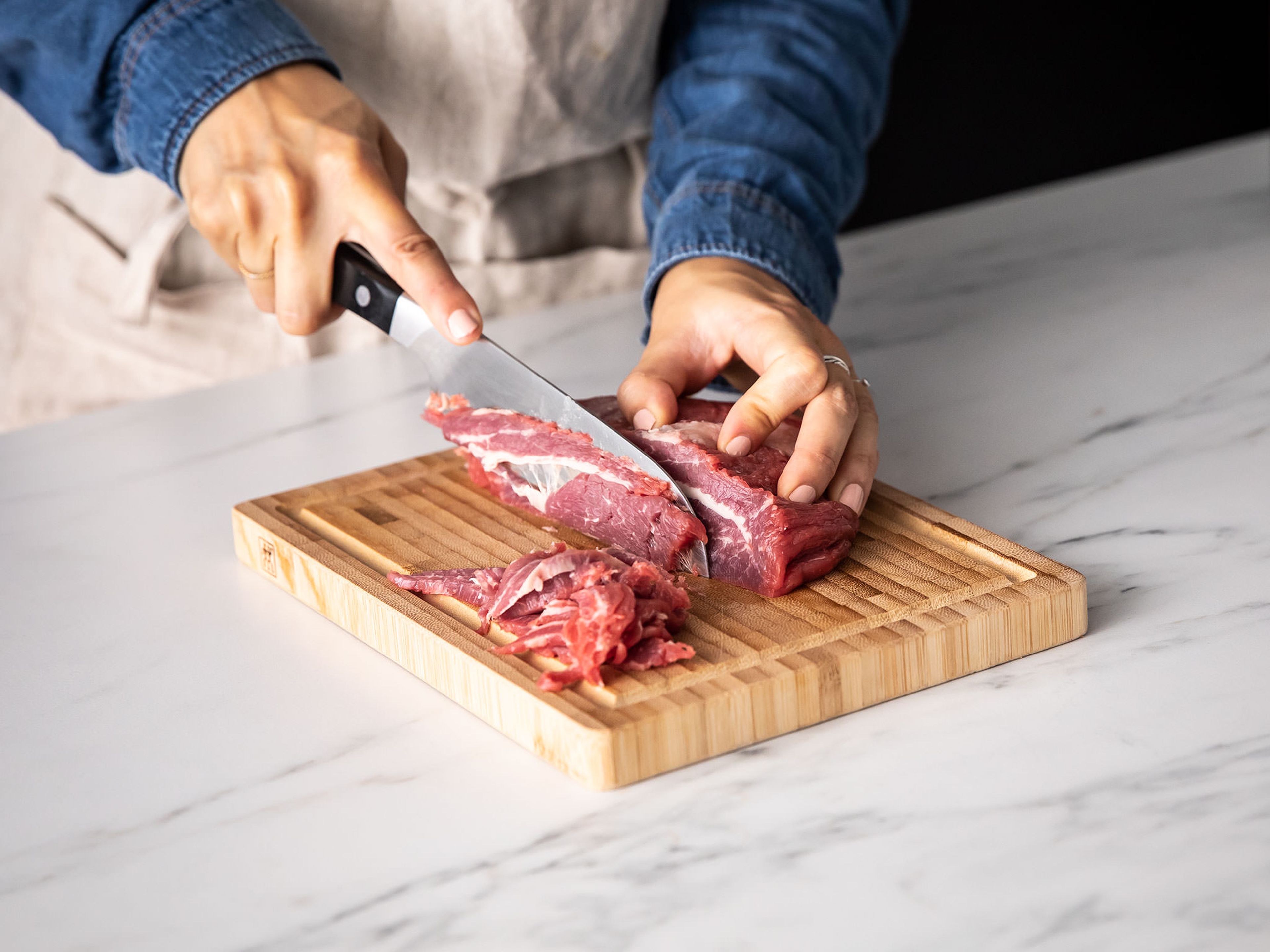 Transfer the meat to a cutting board and freeze for approx. 20 min. In the meantime, peel the onions, core the bell peppers, and thinly slice them both. Then slice the meat as thinly as you can.