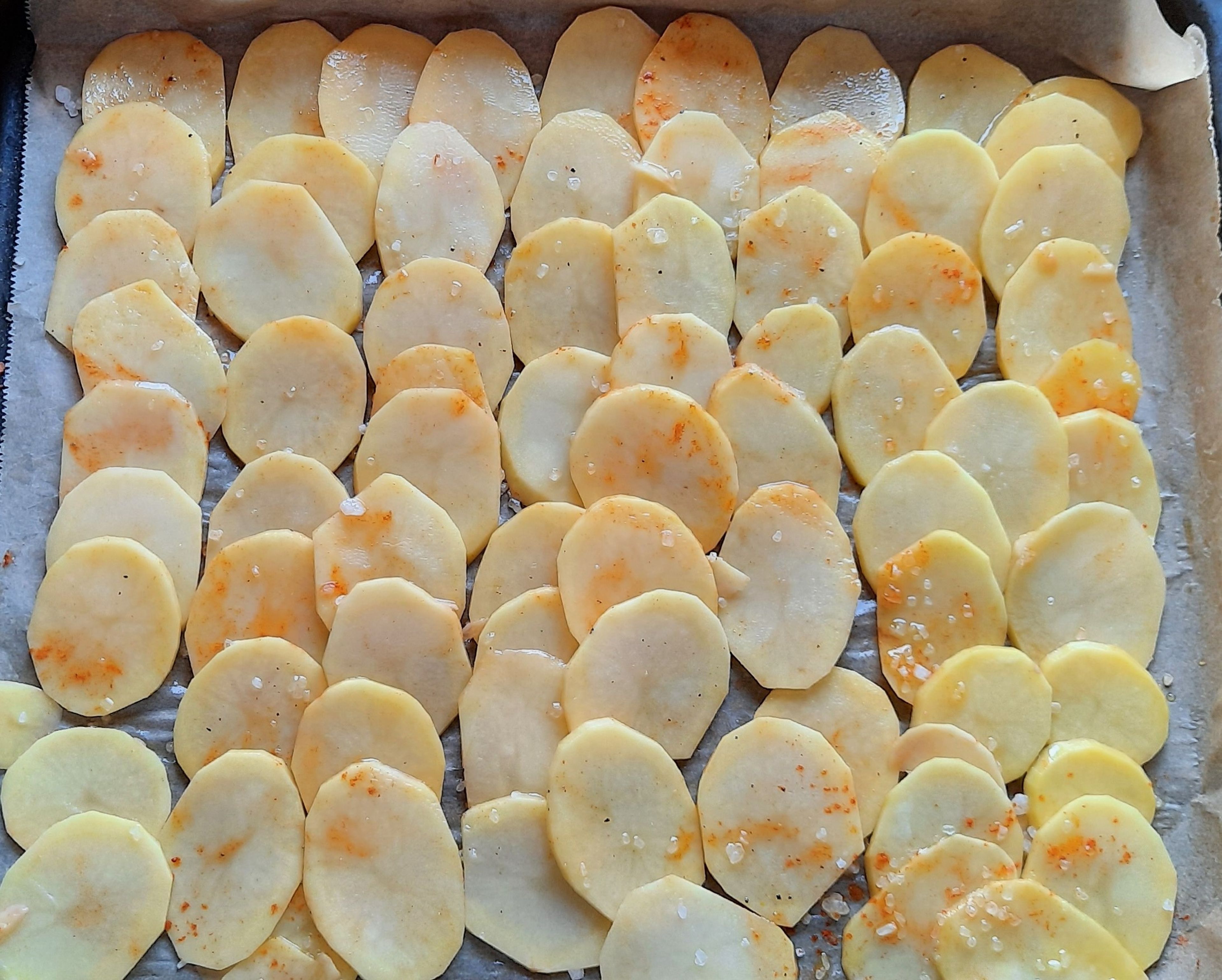 Die Kartoffelscheiben mit Olivenöl, Salz, Pfeffer und Paprikapulver würzen und auf ein Blech legen.