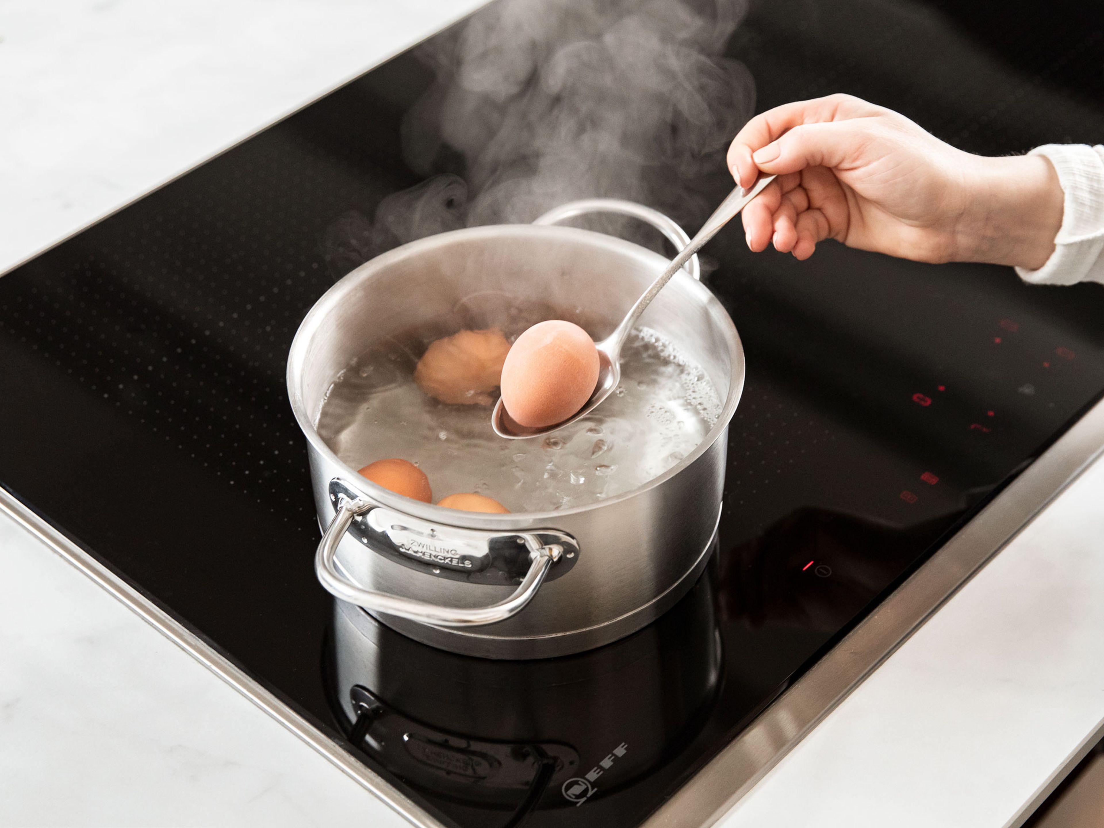 In der Zwischenzeit Wasser in einem Topf zum Kochen bringen. Die Eier vorsichtig in das Wasser geben. Den Deckel daraufsetzen und die Eier bei reduzierter Hitze für ca. 9 Min. kochen, bis sie hartgekocht sind. Nach der Kochzeit die Eier in einer Schüssel mit eiskaltem Wasser abschrecken.