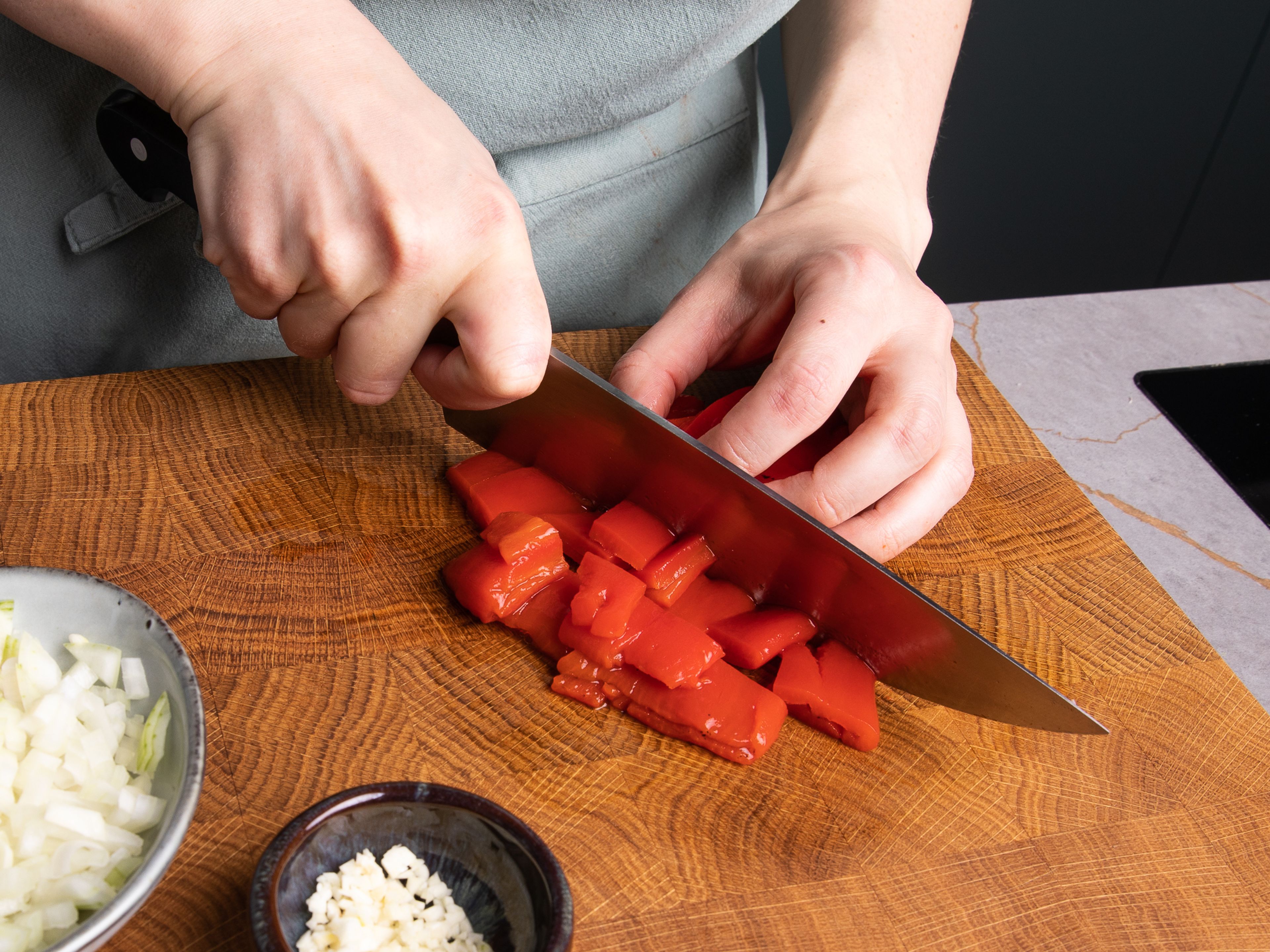 Geröstete Paprika abtropfen lassen und in mundgerechte Stücke schneiden. Zwiebel würfeln und Knoblauch hacken. Bohnen aus der Dose durch ein Sieb gießen, abspülen und abtropfen lassen.
