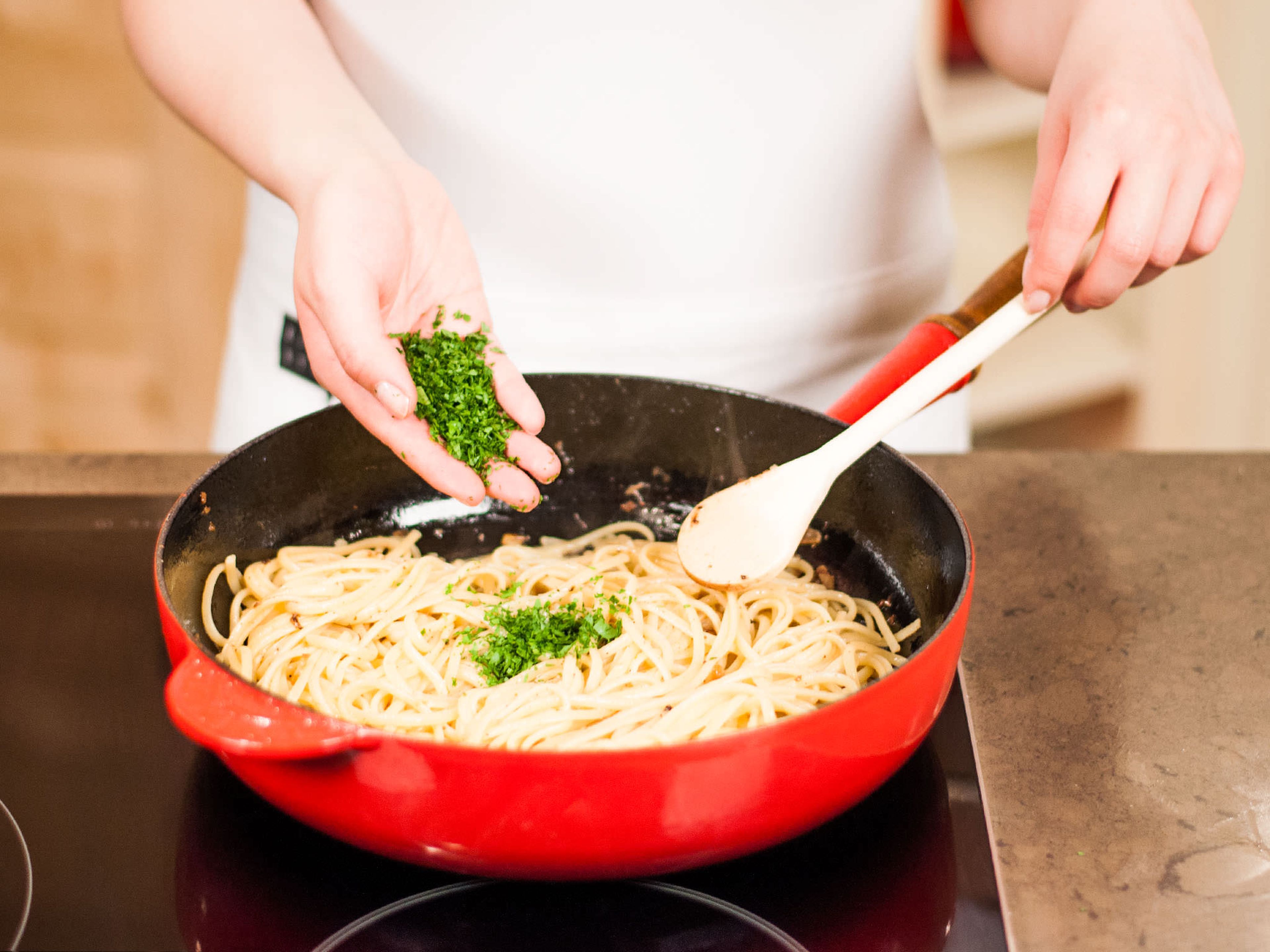 Gekochte Pasta zum Knoblauchöl in die Pfanne geben und darin schwenken. Gehackte Petersilie unterheben und mit Salz und Pfeffer würzen. Nach Belieben mit frisch geriebenem Parmesan servieren.
