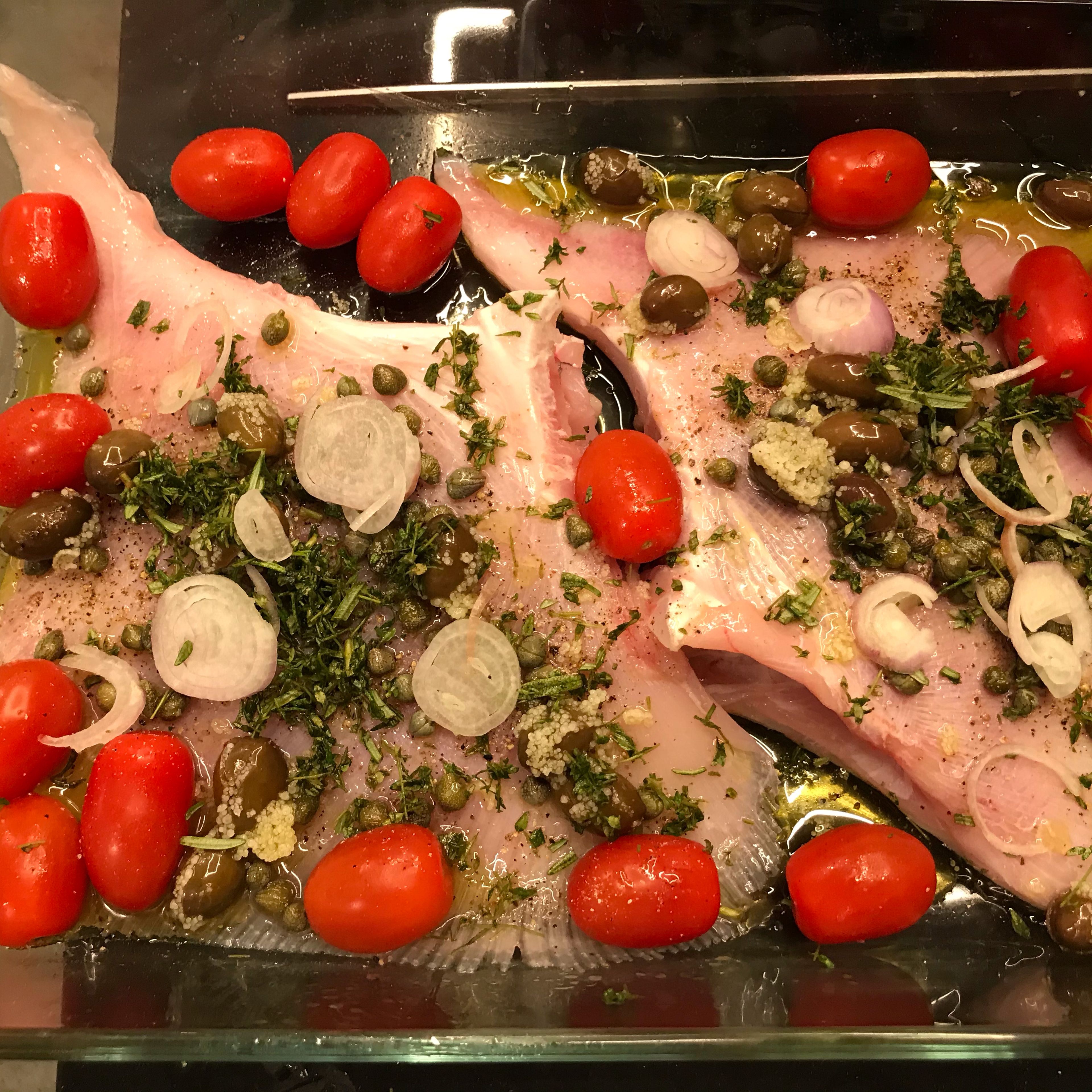 Add the sliced shallot, the crushed garlic, rosemary, thym, tomatoes, olives and capers on top of the skates. Place on the oven for 15-20min.