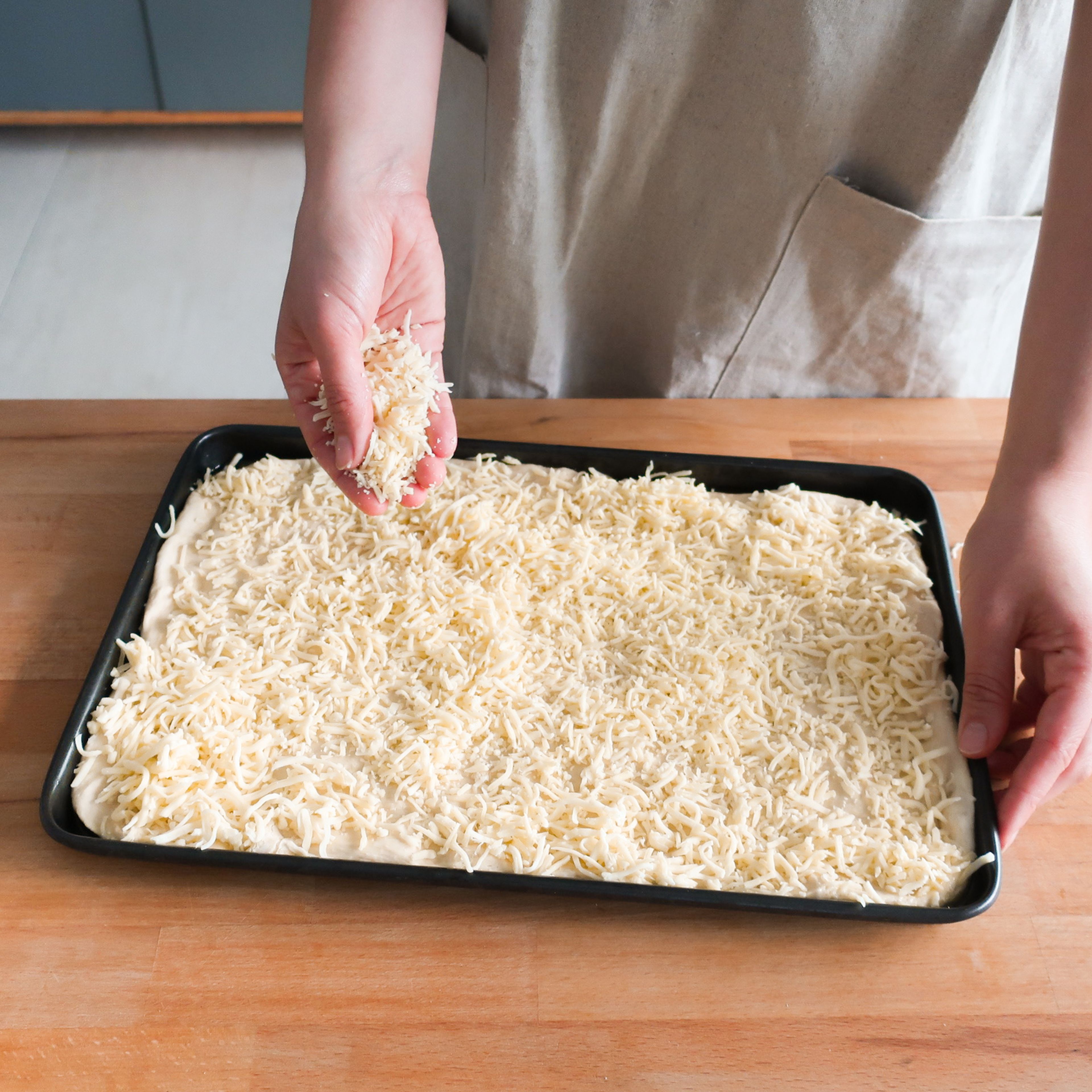 Den Ofen auf 240°C vorheizen oder die Pizza-Einstellung deines Ofens verwenden. Ein Backblech großzügig einölen. Jetzt den Pizzateig auf das Backblech geben und vorsichtig in alle Ecken drücken, bis das Blech komplett ausgefüllt ist. Eine großzügige Schicht geriebenen Mozzarellakäse über die gesamte Teigfläche streuen.