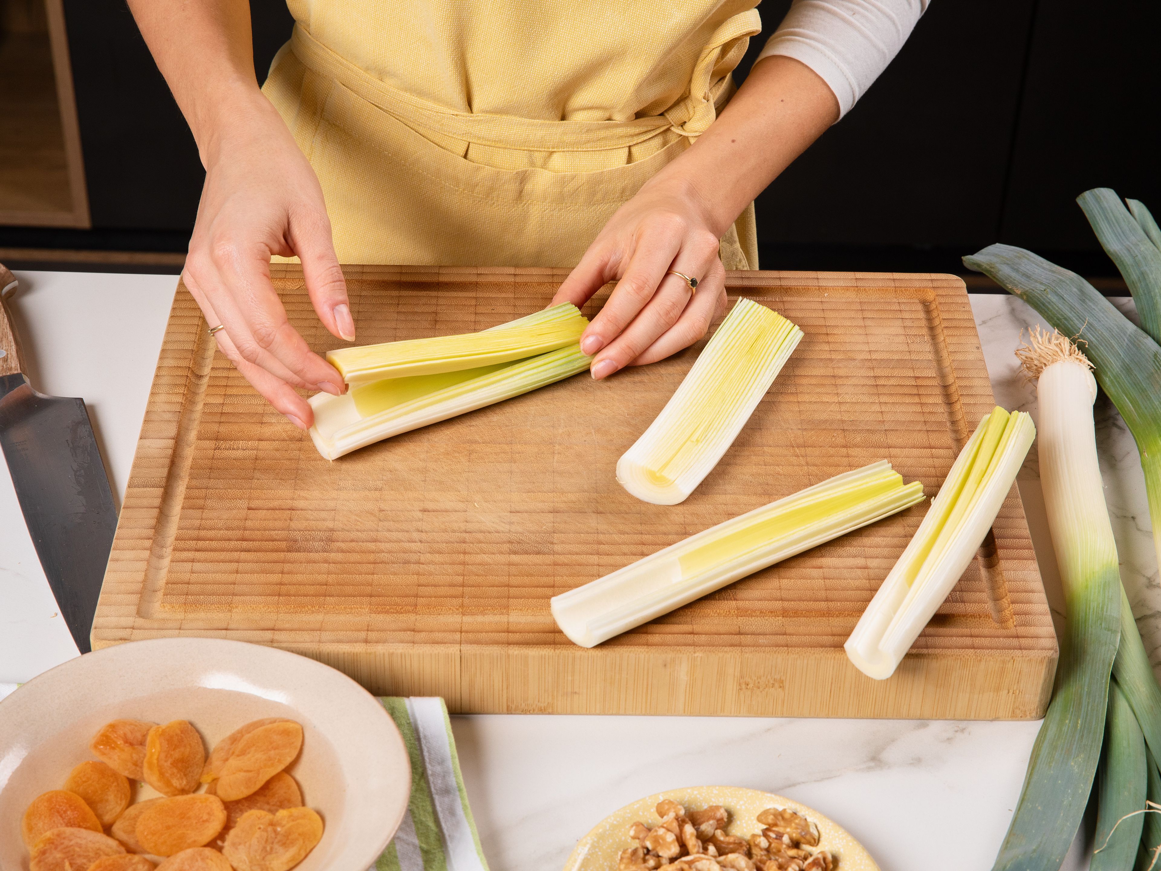 Backofen auf 200 °C vorheizen. Aprikosen in warmem Wasser ca. 10 Min. einweichen, dann abtropfen lassen. Von den Lauchstangen das obere Grün und den Wurzelansatz so abschneiden, dass der innere Kern noch intakt bleibt und der Lauch nicht auseinanderfällt. Lauch längs halbieren und den festen inneren Kern vorsichtig herausschneiden. Aus dem entfernten Inneren feine Streifen schneiden und für später beiseitestellen.