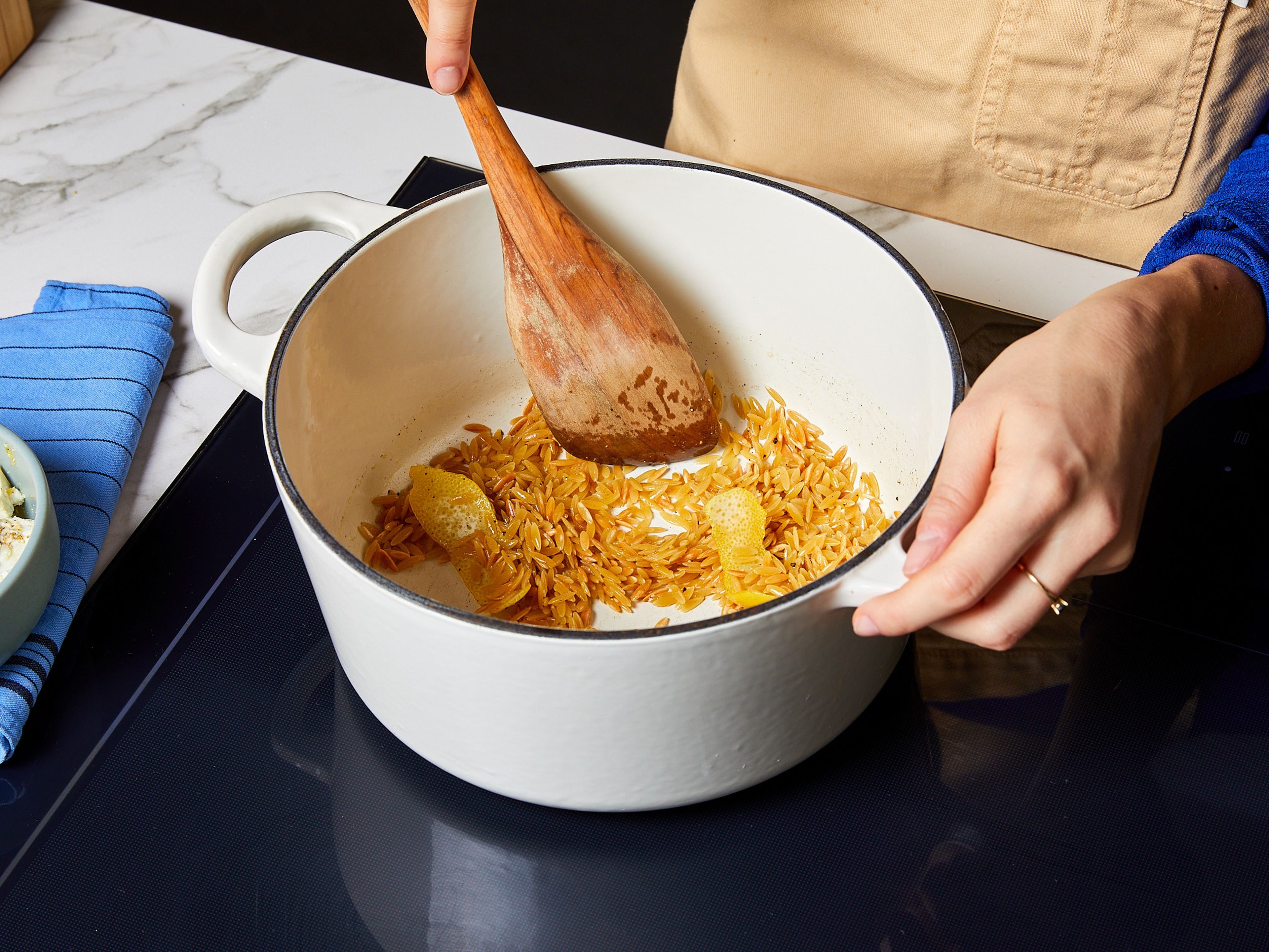 Olivenöl in einem großen Topf erhitzen. Orzo bei mittlerer Hitze etwas anrösten, bis er leicht goldbraun wird (Wer möchte, kann etwas Zitronenschale hinzugeben). Orzo aus dem Topf nehmen und beiseite stellen. Im selben Topf das Hähnchen mit etwas Olivenöl von beiden Seiten für je ca. 2 Min. anbraten, bis es goldbraun ist, dann herausnehmen.