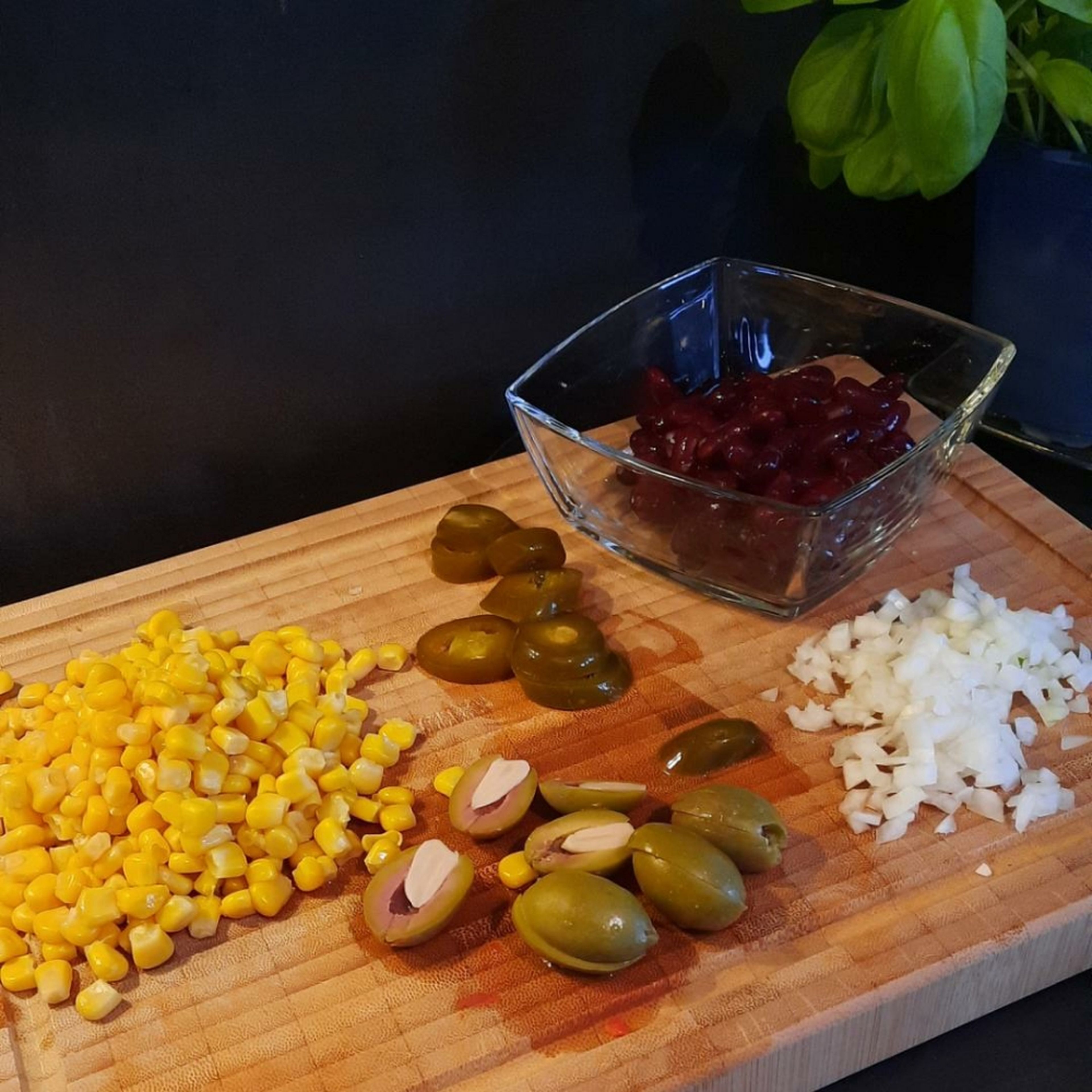 Zwiebel in Würfel schneiden, Oliven halbieren, Jalapeños, Bohnen und Mais abtropfen lassen.