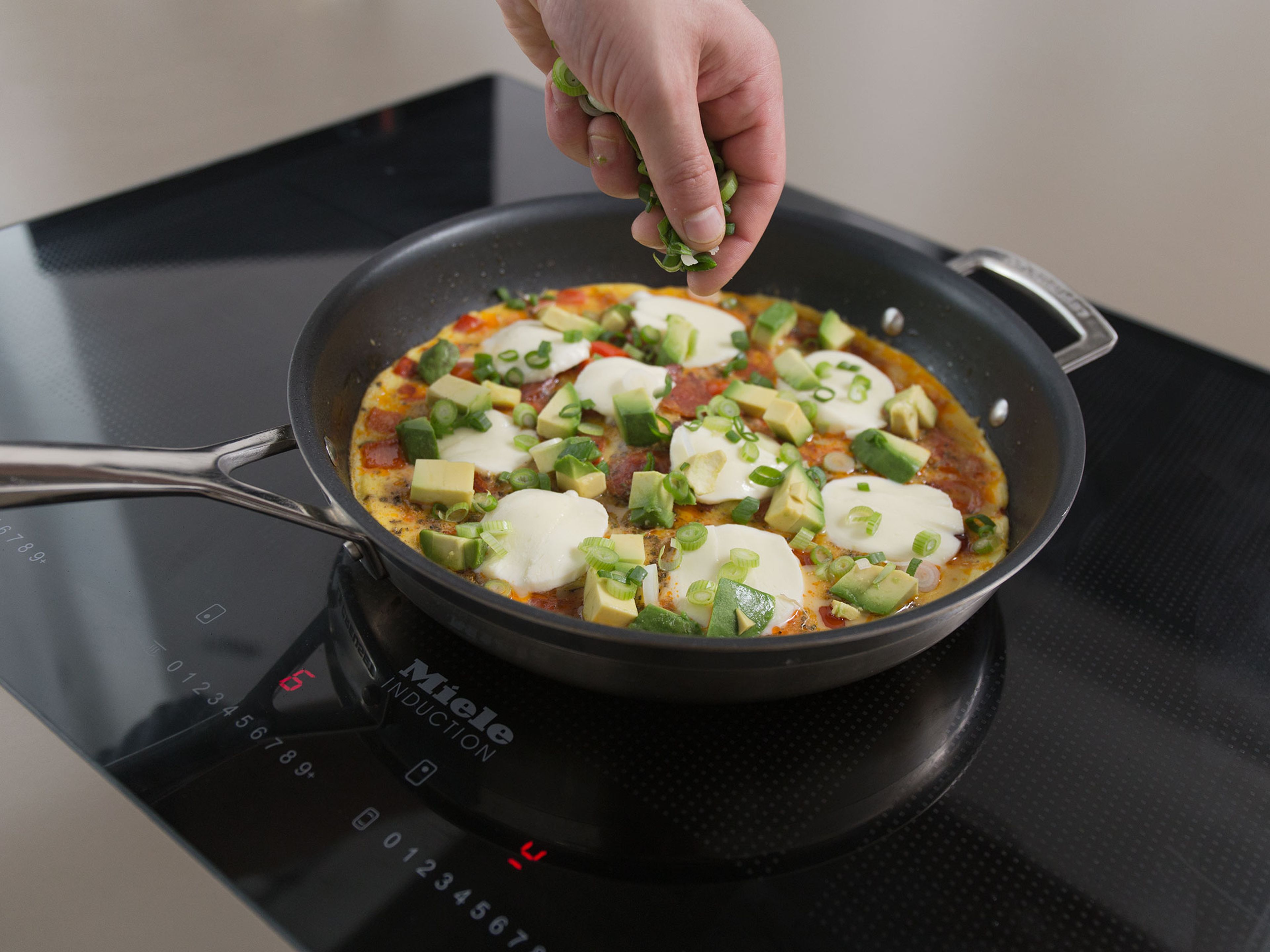 Sobald das Omelett zur Hälfte gestockt ist Avocado, Mozzarella und Frühlingszwiebeln darüber streuen. Deckel darauf setzen und ca. 2 Min. weiterkochen lassen. Mit restlicher Petersilie bestreuen. Guten Appetit!
