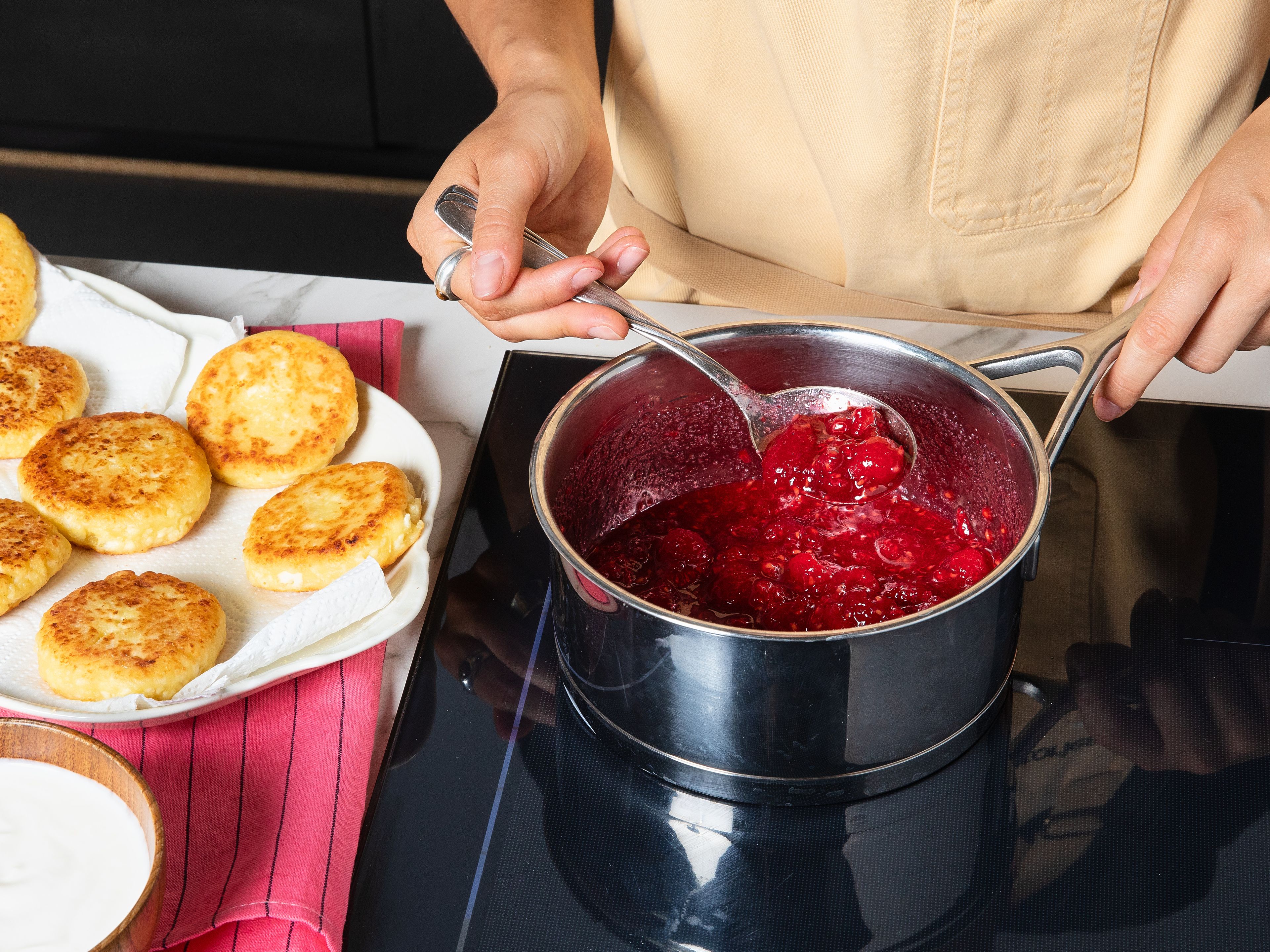 For the sauce, add raspberries and sugar to a small saucepan and bring to a boil. Let simmer for a few minutes until slightly thickened. Stir sour cream with a bit of sugar until smooth. Serve the syrniki warm with sweetened sour cream and raspberry sauce, and garnish with fresh berries if desired.