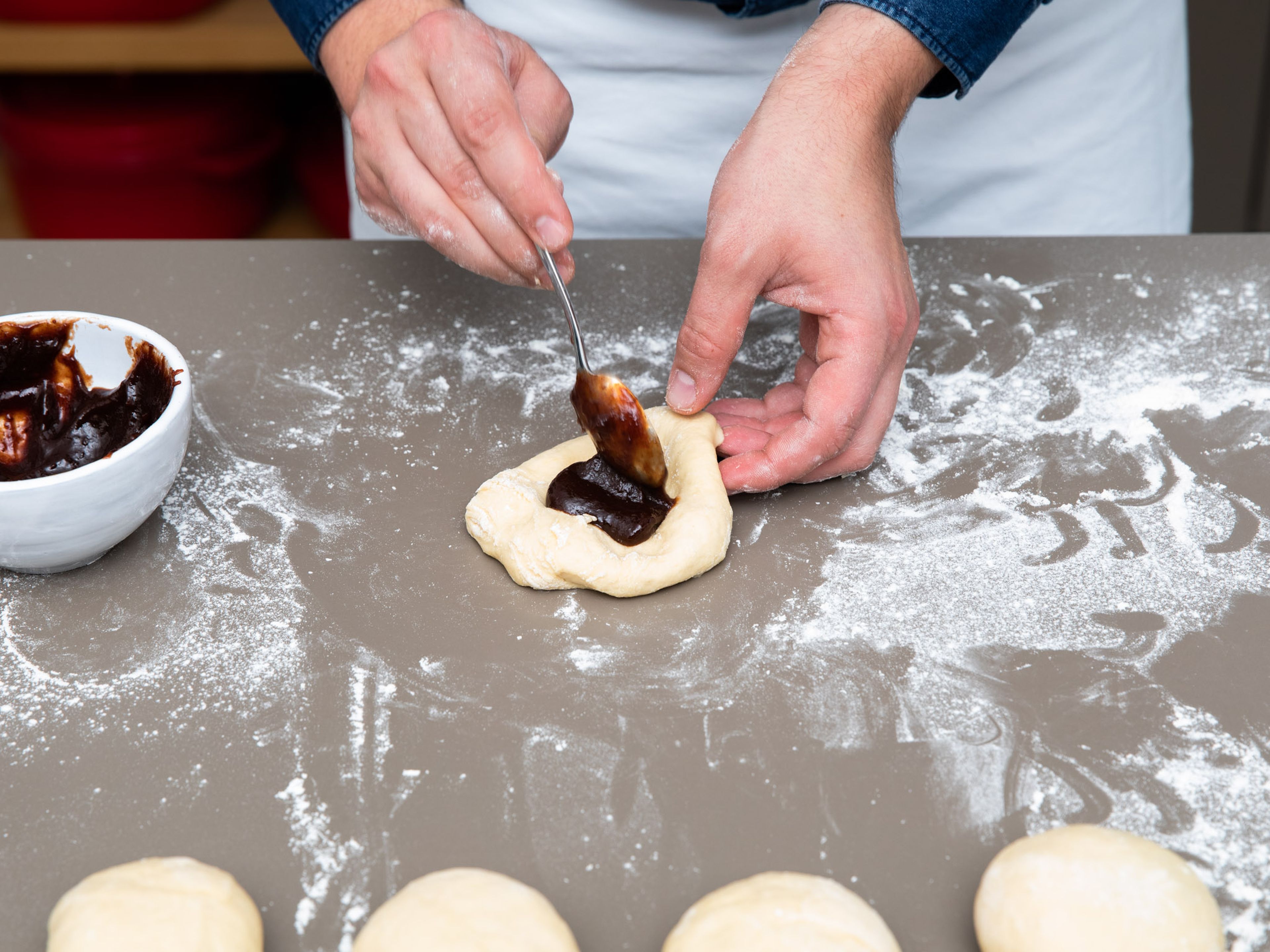 Flour your work surface and divide the dough into 8 equal-sized pieces. Form each dough piece into a disc, add a tablespoon of plum jam into the center of the disc and fold dough gently over the filling, pinching the seam. Form into round dumplings and let rest again for approx. 15 min.