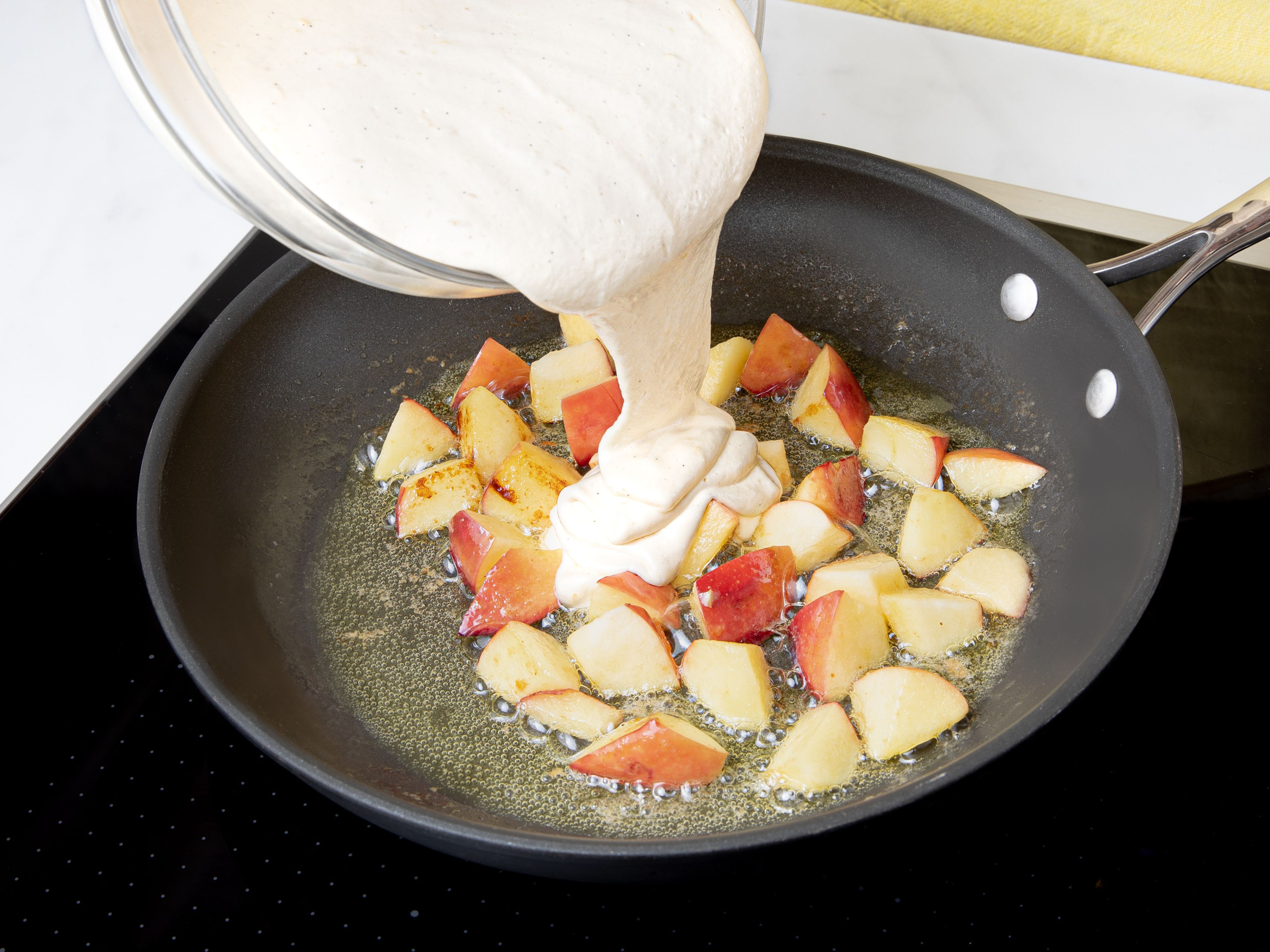 Backofen auf 200°C Umluft mit Grill vorheizen. Die Hälfte der Butter bei mittlerer Hitze in einer ofenfesten Pfanne schmelzen, Apfelstücke zugeben und für ca. 3 Min. andünsten. Die Hitze etwas reduzieren und den Teig auf die Äpfel in die Pfanne geben. Mandelstifte und Rosinen darüberstreuen.