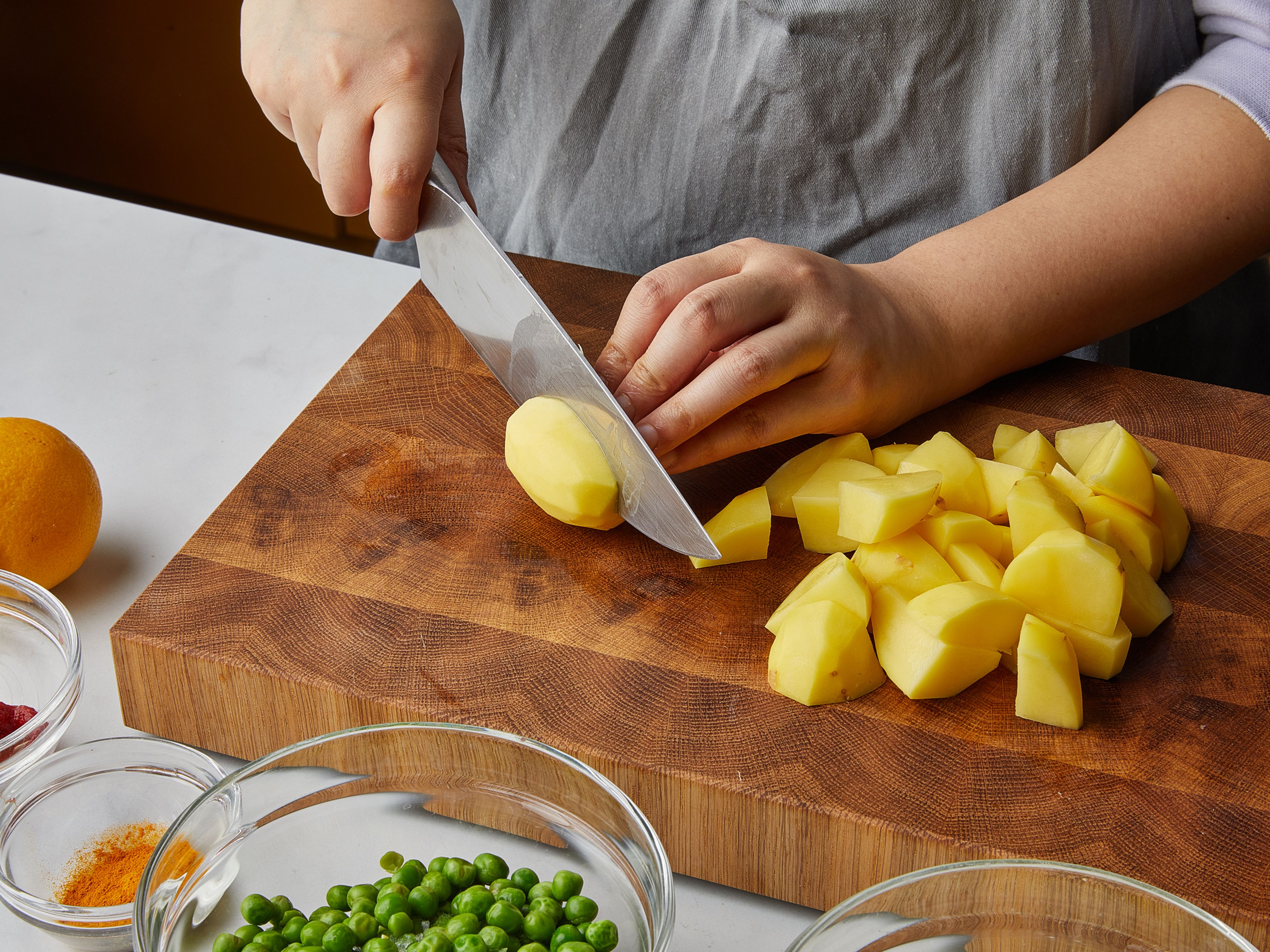Die Zwiebel fein würfeln. Dann die Knoblauchzehen mit der flachen Seite des Messer zerdrücken. Den Ingwer hacken und die Chilis fein schneiden. Anschließend die Kartoffeln schälen und vierteln.