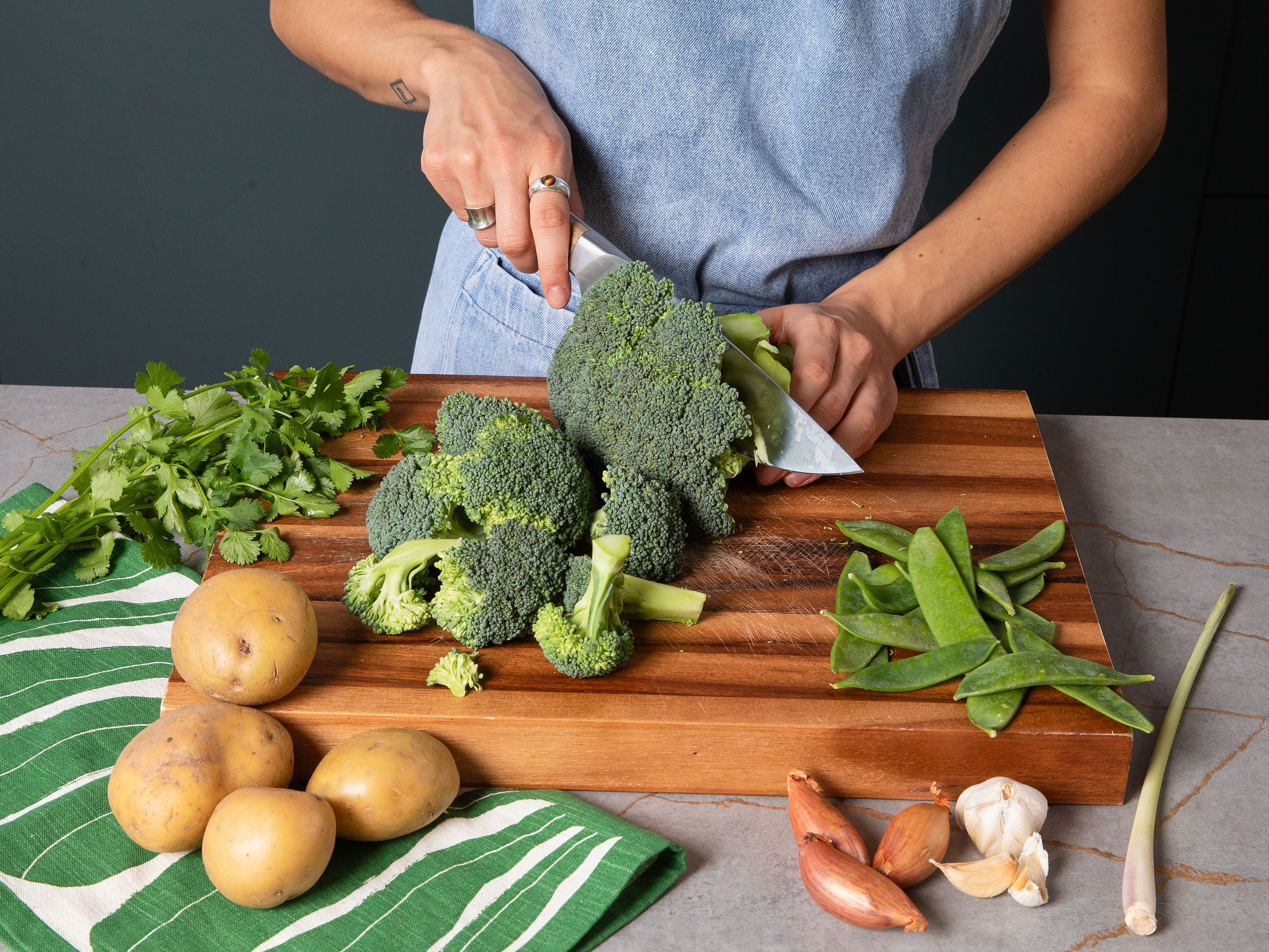 Backofen auf 200 °C Ober-/Unterhitze vorheizen. Brokkoli in kleine Röschen teilen. Kartoffeln in Würfel schneiden. Die äußere, holzige Schicht des Zitronengrases entfernen, dann in feine Ringe schneiden. Schalotten in feine Ringe schneiden. Knoblauch und Ingwer schälen. Ein paar Korianderblätter zum Garnieren beiseite legen, den Rest samt Stielen grob hacken. Limetten auspressen.