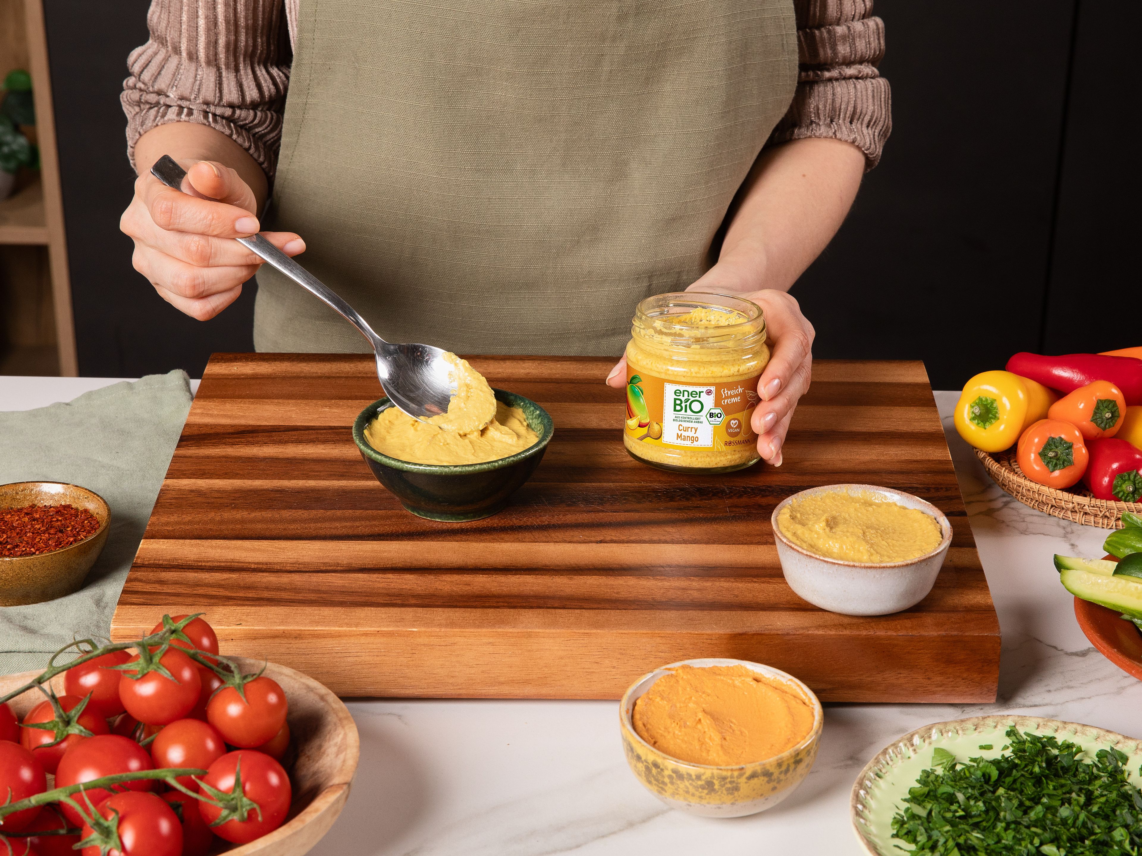 Währenddessen die rote Zwiebel in dünne Ringe schneiden. In eine kleine Schüssel geben und mit Zitronensaft, Sumak sowie einer Prise Salz und enerBiO Rohrohrzucker vermengen und ca. 10 Min. ziehen lassen. Mini-Gurken in handliche Sticks schneiden, Feta würfeln und Petersilie grob hacken. Die enerBiO Curry Mango Streichcreme, den enerBiO Tomate Parmesan Streichgenuss und die enerBiO Edamame Hummus Art Streichcreme in kleine Schälchen füllen und jeweils mit etwas Olivenöl, Chiliflocken, Petersilie oder Sumak verfeinern.