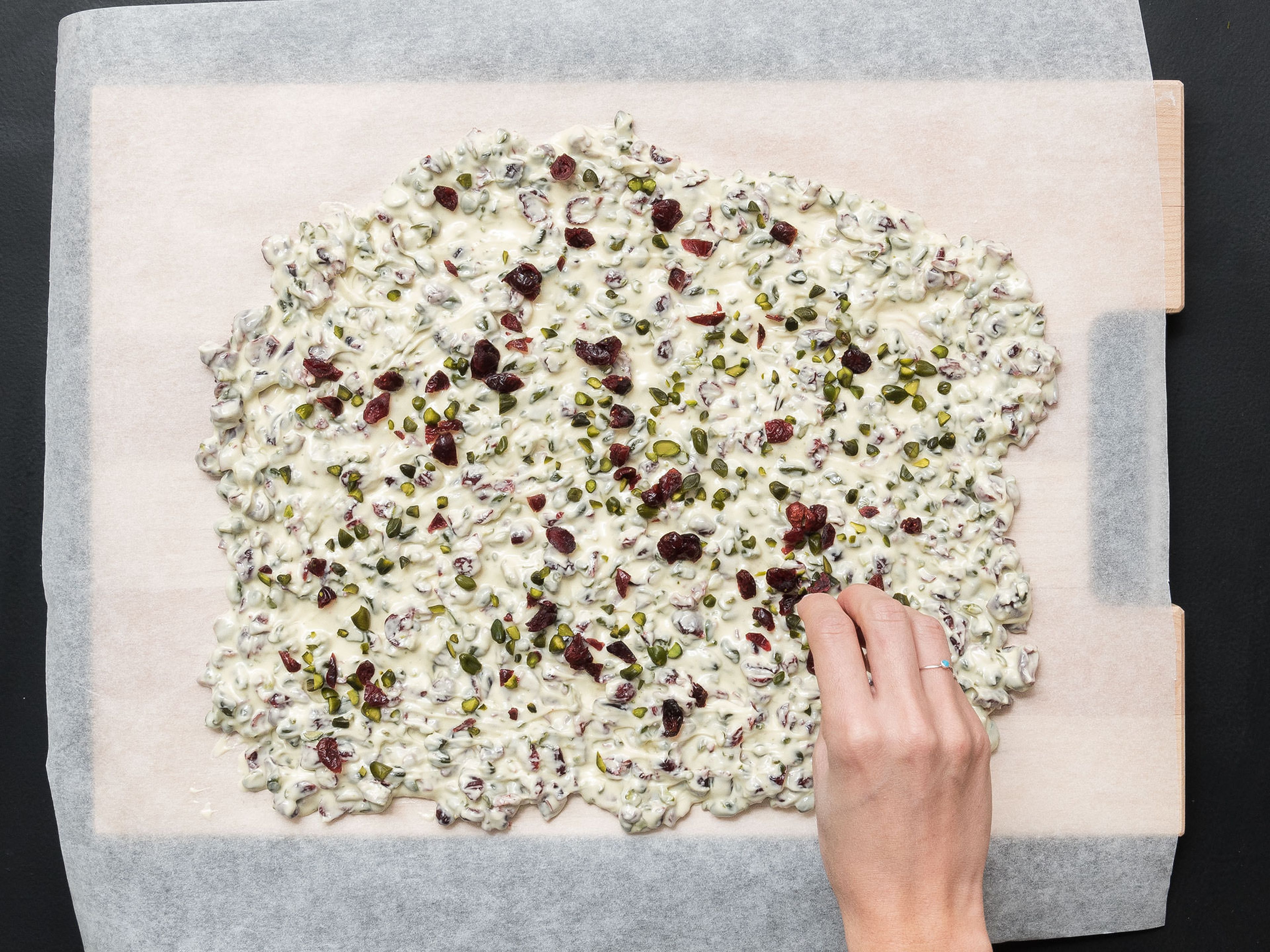 Spread the chocolate mixture over parchment paper, approx. 0.5-cm/0.25-in. thick, and sprinkle remaining pistachios and cranberries on top.