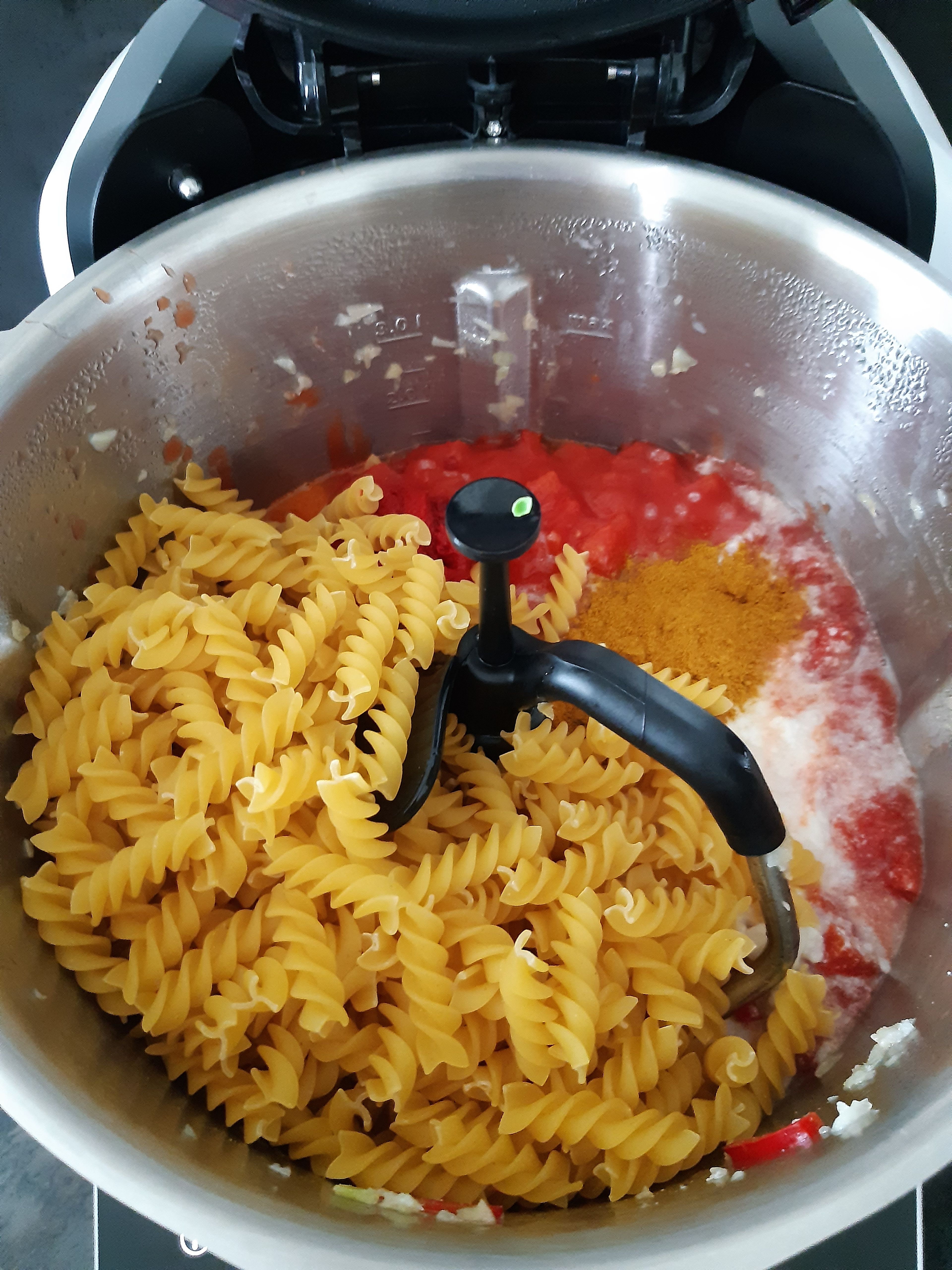 Die stückigen Tomaten, die Kokosmilch, Fusilli, Tomatenmark und das Curry hinzufügen und alles bei geschlossenem Deckel, ohne Messbecher, kochen (3D-Rührer | Stufe 2 | 95°C | 20 Minuten).