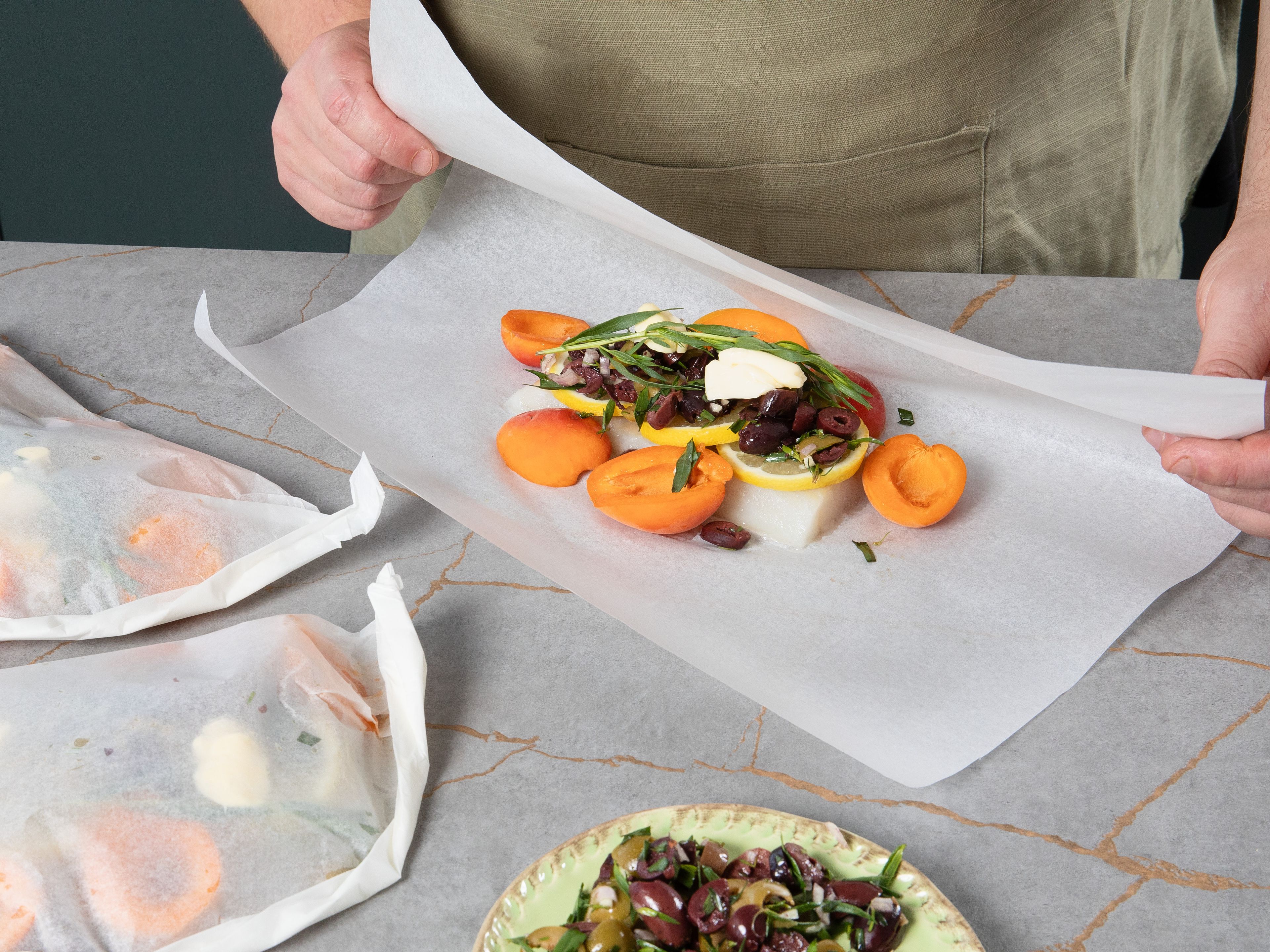 For each packet, place cod and a quarter of the apricots on one half of a large piece of parchment paper. Top with a quarter of each lemon slices, olive mixture, tarragon, and a piece of butter. Fold other half of parchment paper over fish and fold edges together until a small packet is completely sealed.