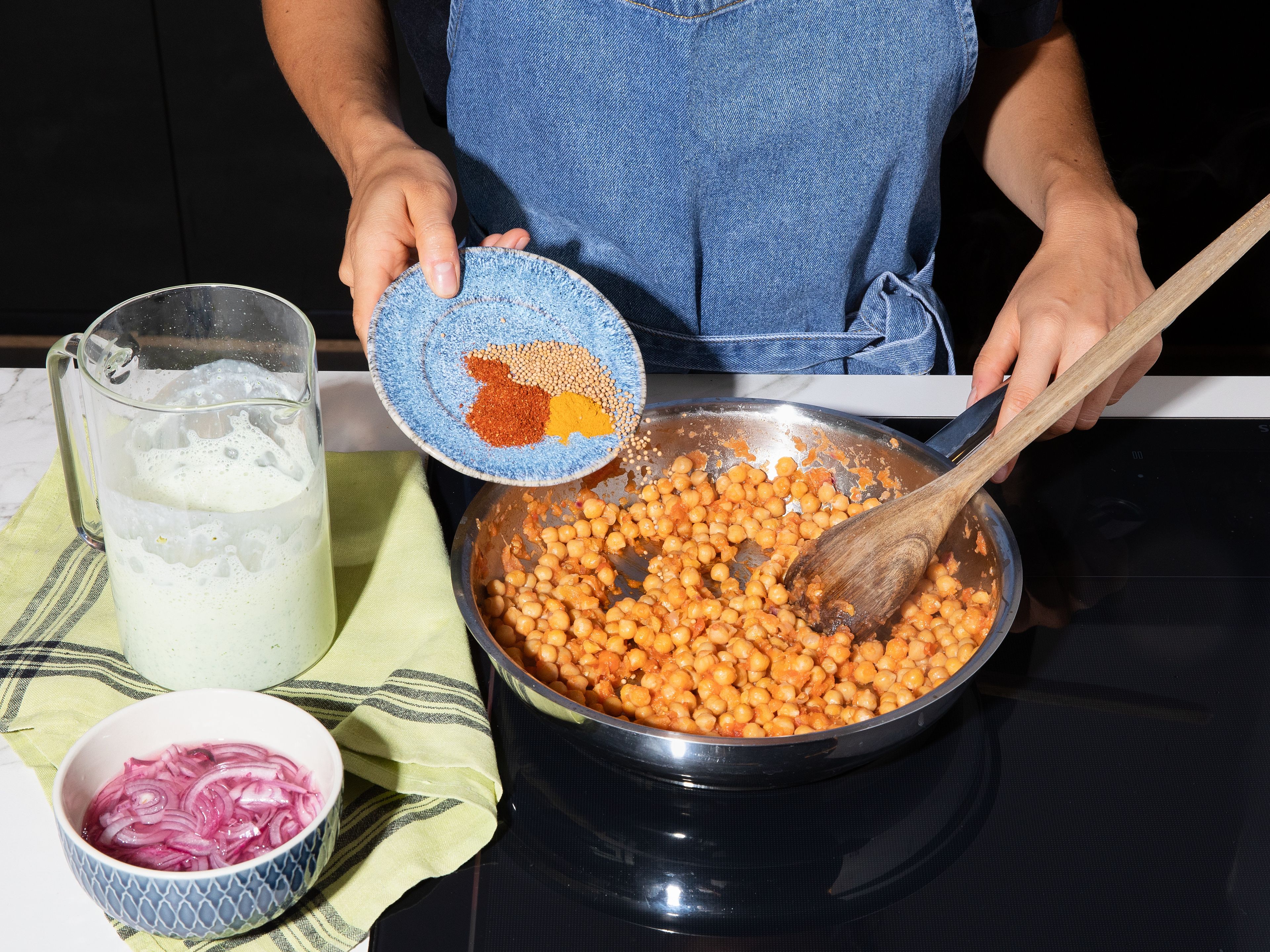 Kichererbsen abspülen und abtropfen lassen. Tomate, Zwiebel, Knoblauch und Ingwer fein reiben oder hacken. Etwas Öl in einer großen Pfanne erhitzen und die Mischung darin anschwitzen, bis die Flüssigkeit verkocht ist. Kichererbsen hinzufügen, mit Salz und Pfeffer würzen und ca. 3–5 Min. anbraten. Mit Tandoori-Gewürz, Senfkörnern und Kurkuma würzen und alles weitere ca. 2 Min. braten.