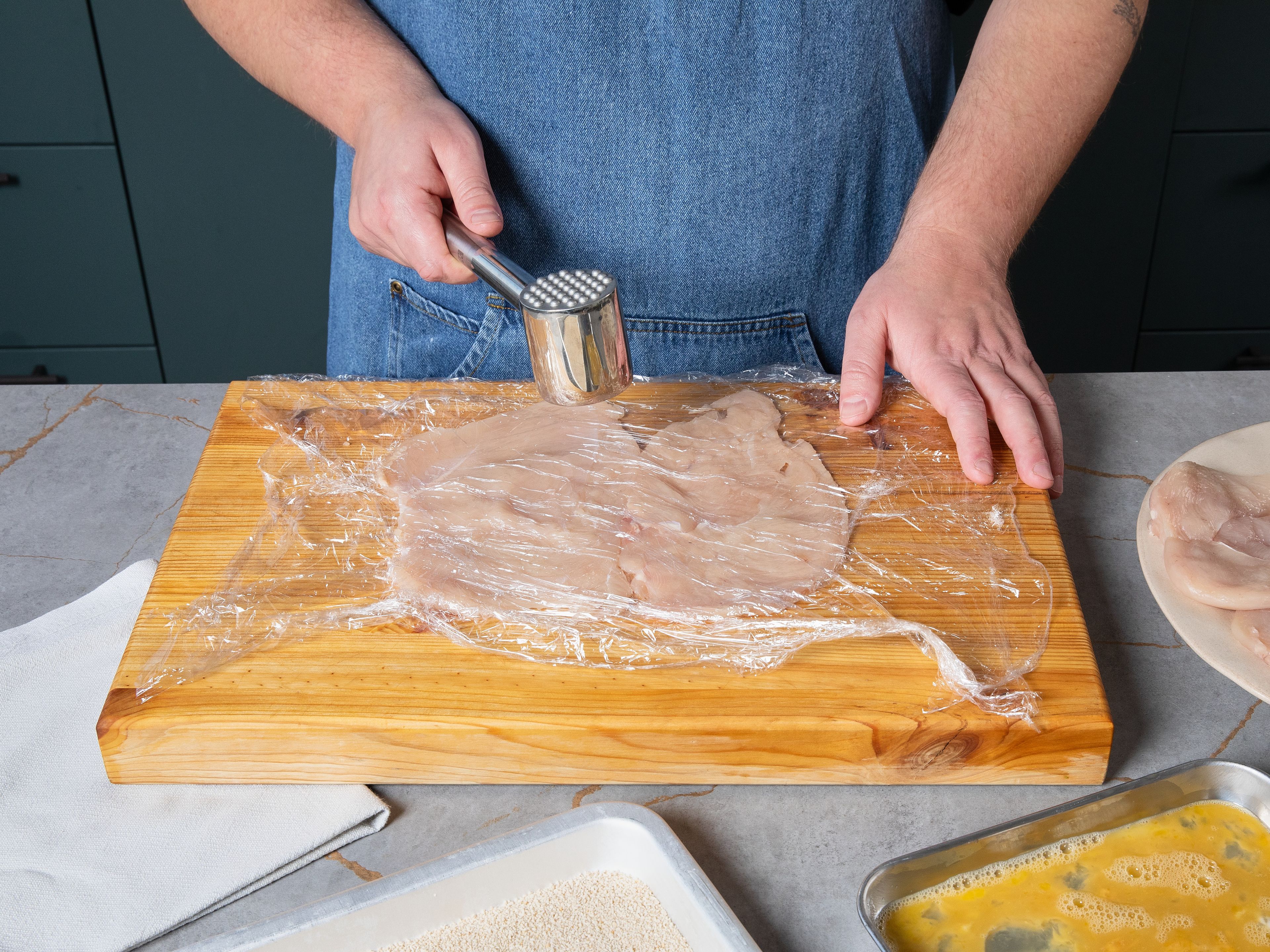 Die Hähnchenfilets der Länge nach aufschneiden, aber nicht komplett durchtrennen, und auseinanderklappen. Anschließend das Fleisch zwischen zwei Lagen Frischhaltefolie legen und mit einem Fleischklopfer oder einem kleinen Topf dünn klopfen.