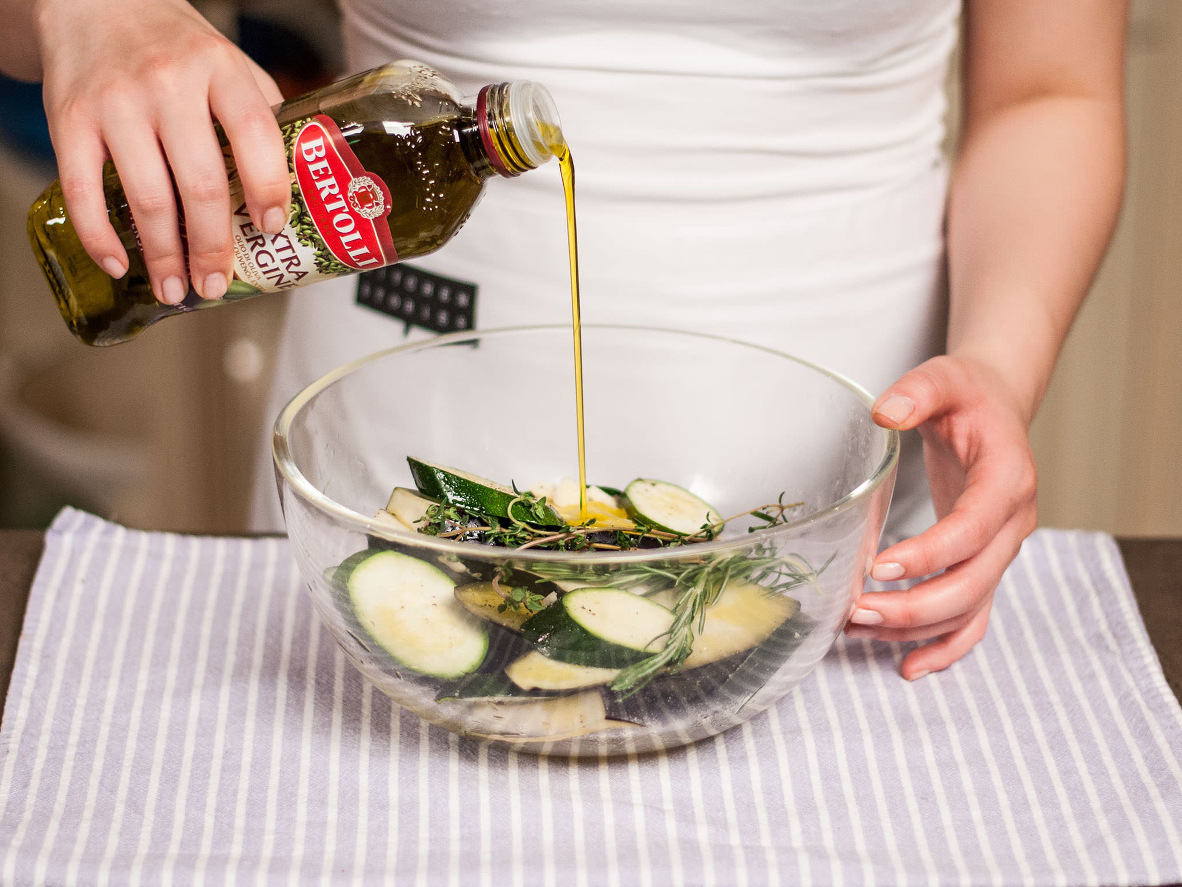 In einer großen Schüssel die Auberginen- und Zucchinischeiben in Olivenöl marinieren. Grob gehackten Thymian und Rosmarin und sowie zerdrückte Knoblauchzehen hinzugeben. Mit Salz und Pfeffer würzen und gut vermengen.