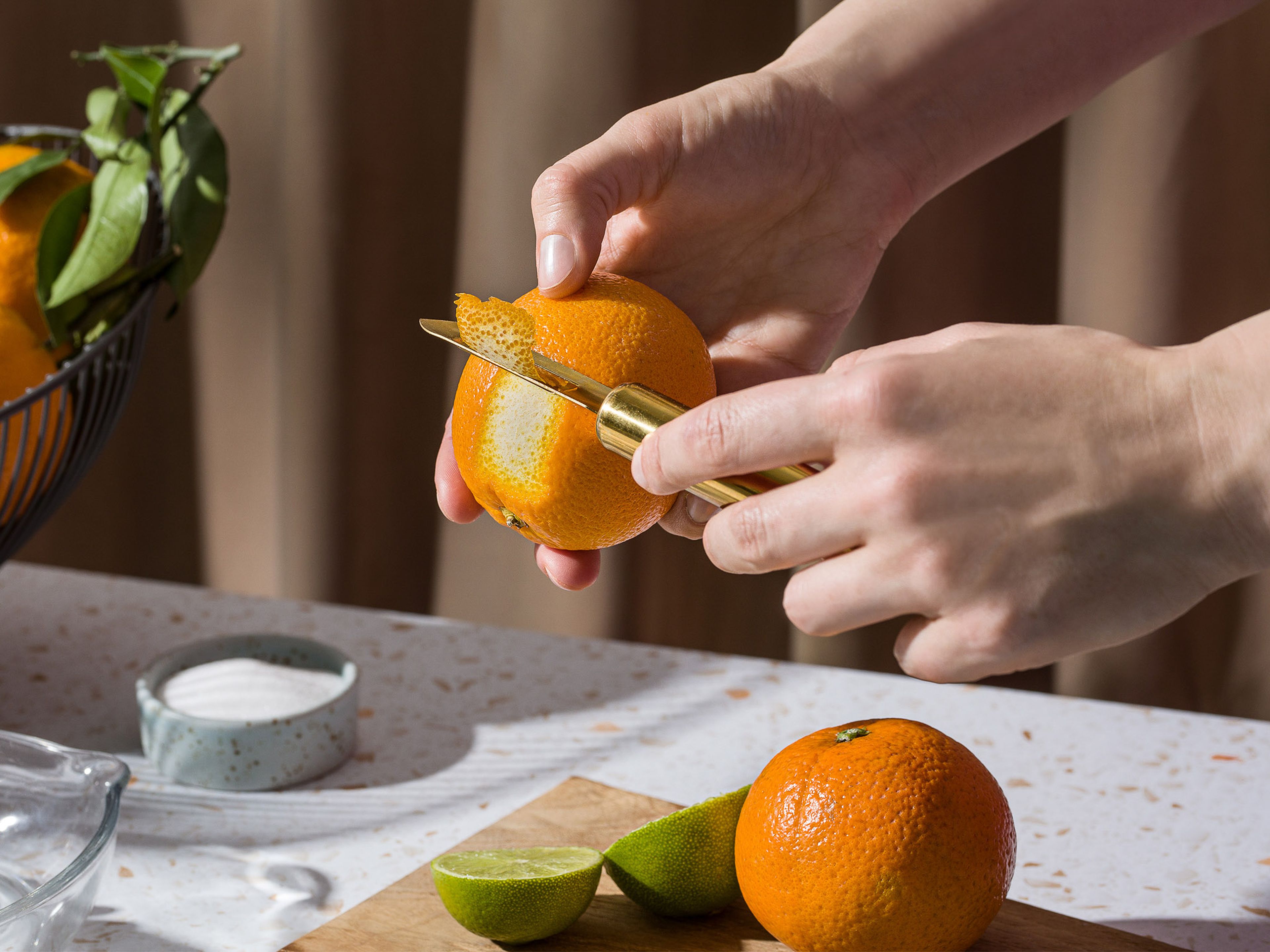 Einen ca. 2 cm dicken Streifen Orangenschale mit einem Sparschäler von einer Orange abziehen und beiseite legen. Orangen halbieren, Saft auspressen. Limetten halbieren, Saft auspressen.