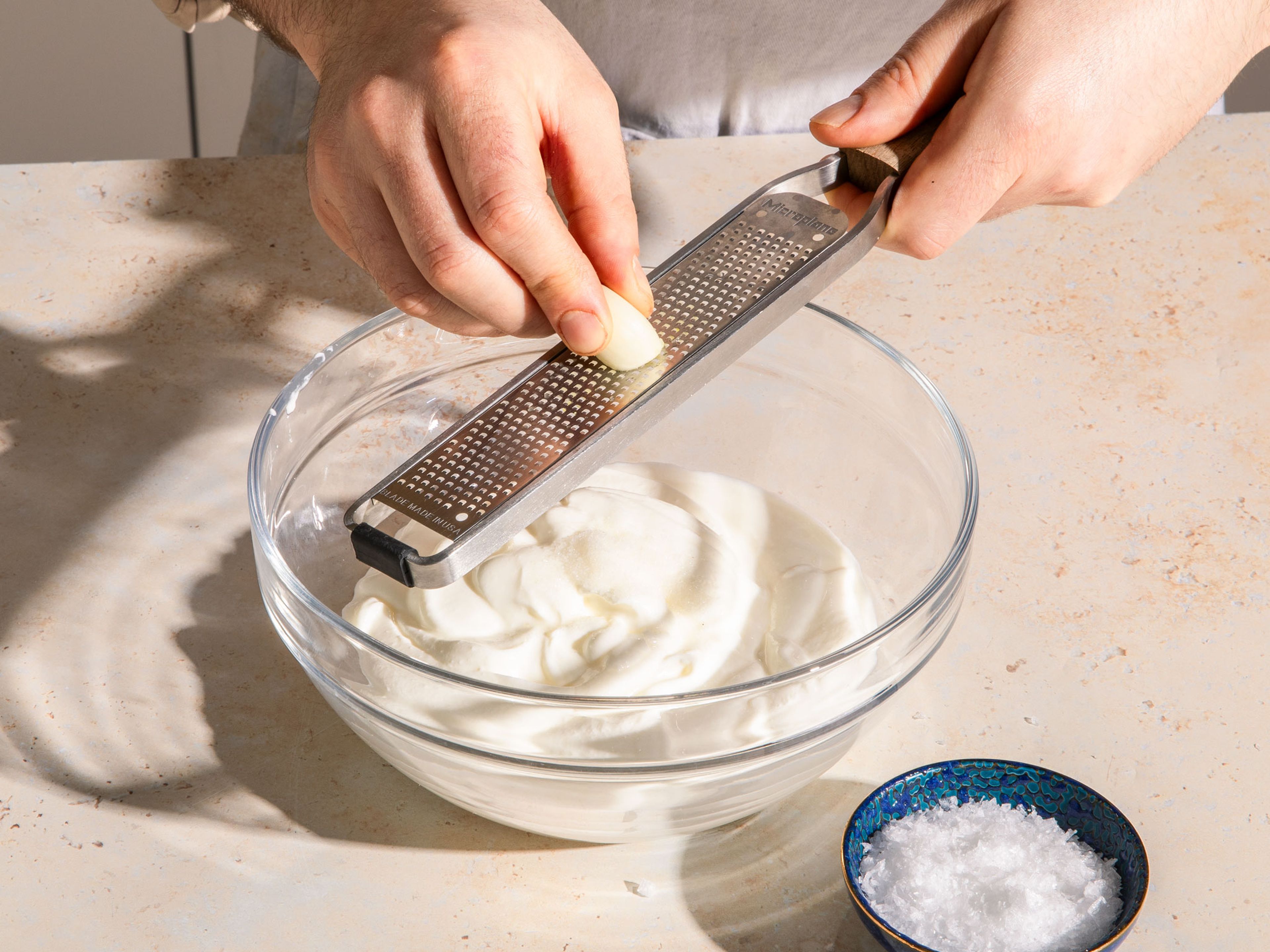 Joghurt in eine Schüssel geben, etwas Salz hinzufügen und Knoblauch mit einer Reibe hineinreiben und umrühren. Den gemischten Joghurt mit einem Küchenspatel in ein sauberes Küchen- oder Käsetuch geben, das Tuch zudrehen und über einer Schüssel zum Abtropfen aufhängen. Dieser Schritt kann auch am Abend vorbereitet und im Kühlschrank aufbewahrt werden.