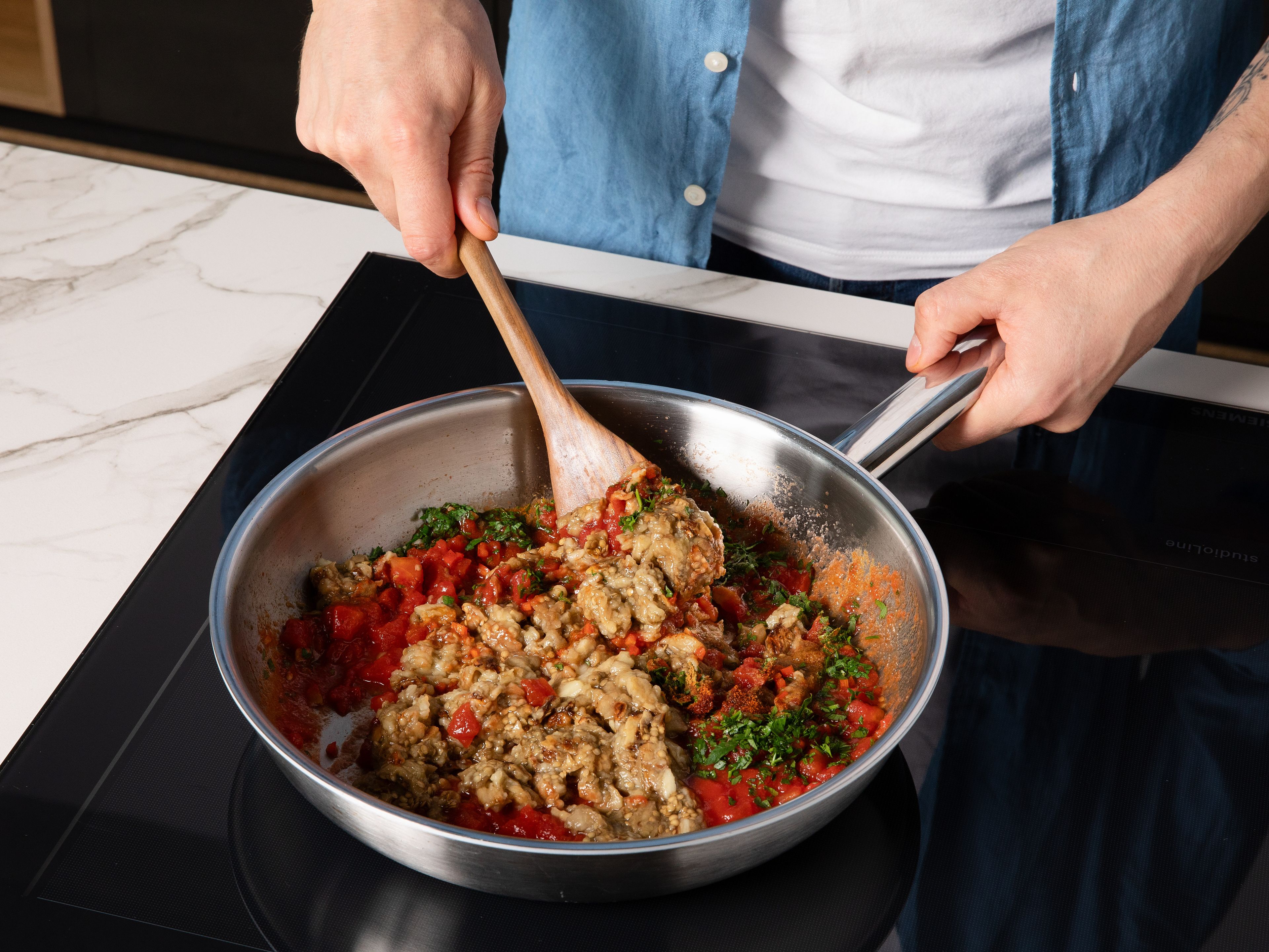 Chili und Kräuter fein hacken. Zitrone halbieren. Die Hälfte des Olivenöls in einer Pfanne erhitzen, Knoblauch kurz anbraten, dann die Tomatenwürfel dazugeben und bei mittlerer Hitze ca. 10 Min. köcheln lassen, bis die Masse eindickt. Auberginen, Kreuzkümmel, Paprikapulver, Petersilie, Koriander und Chili einrühren. Mit Zitronensaft, Salz und Pfeffer abschmecken und ca. 5 Min. weiterköcheln lassen.