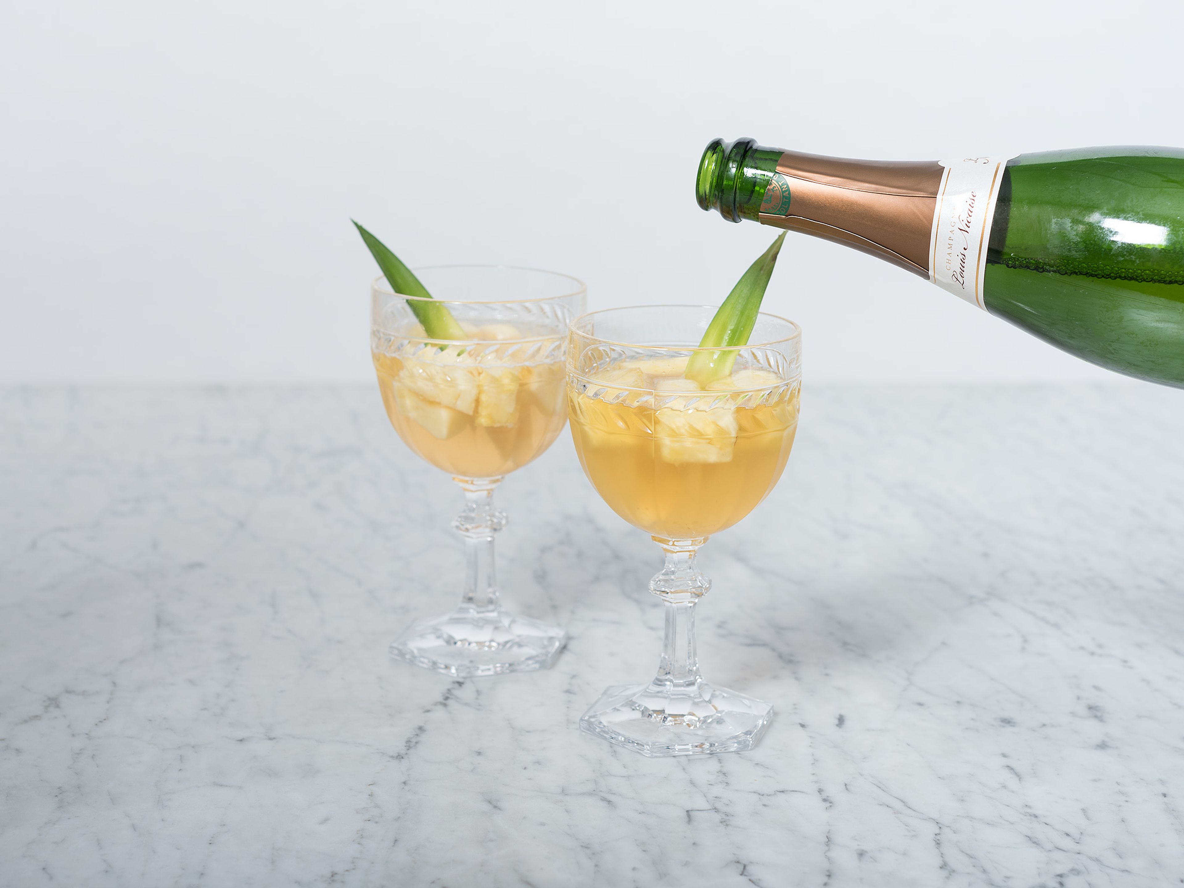 Serve in stemmed glasses, top with Champagne, and garnish with berries and pineapple leaves.  Enjoy!