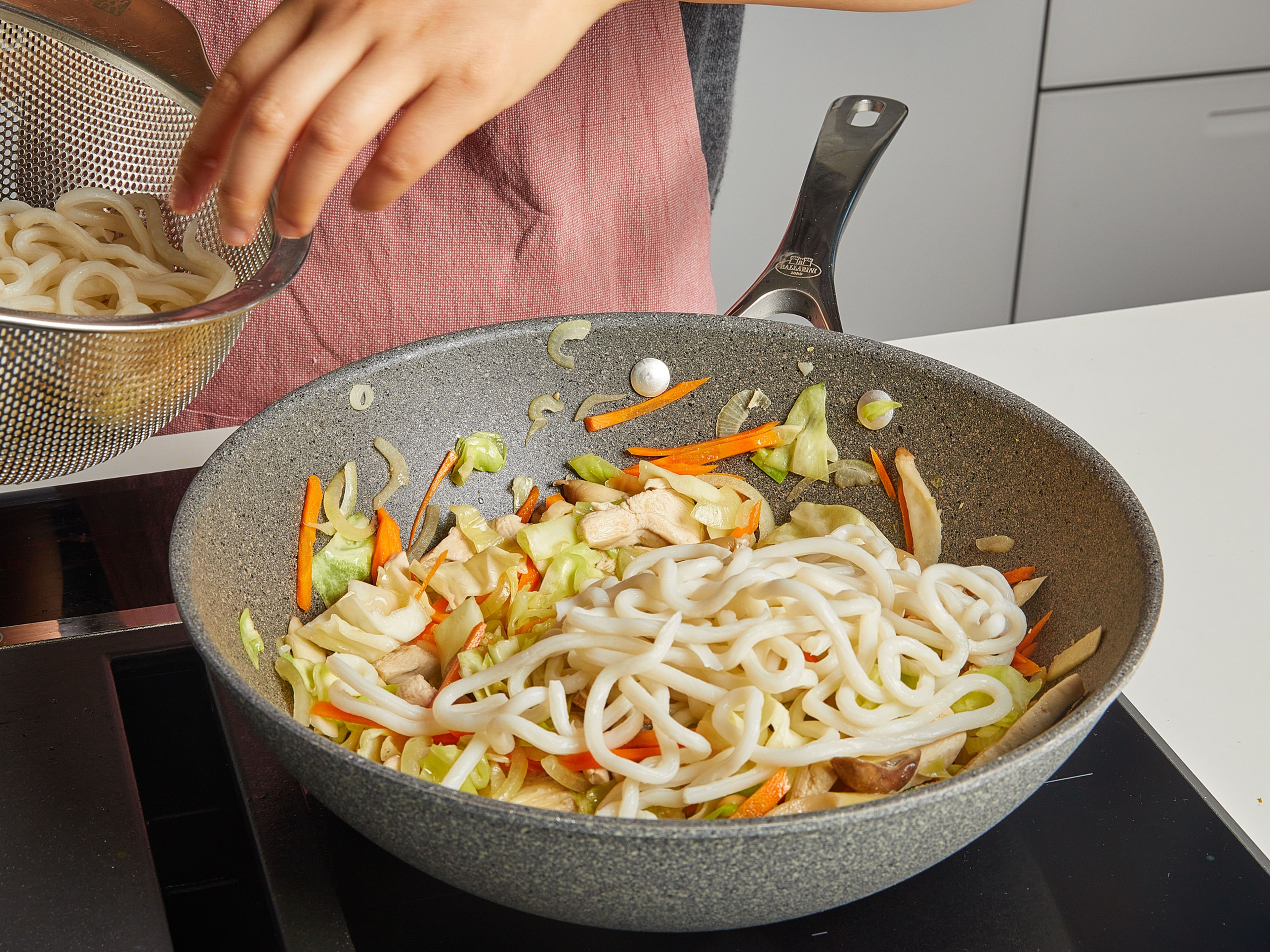 Add your drained, loose udon noodles. Then add the sauce mixture. Stir-fry for approx. 3–5 min. Use a pair of chopsticks to stir-fry the noodles, and mix until the sauce is well combined. Season with salt and pepper, garnish with scallion greens and serve immediately.