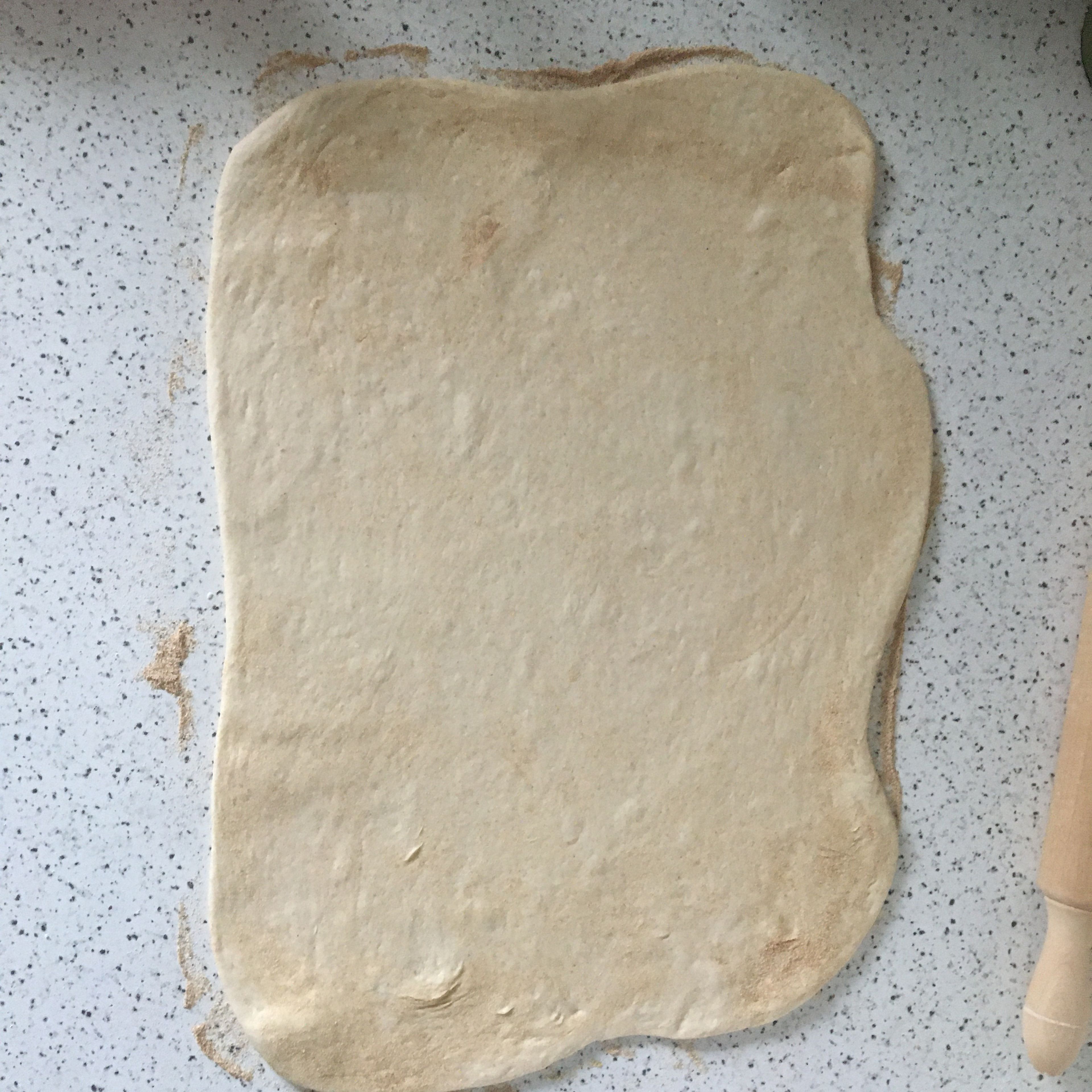 When the dough has risen and doubled in size, carefully transfer it onto a floured work surface and fold for a few times. With the help of a rolling pin and your hands, flatten the dough into a large rectangle.