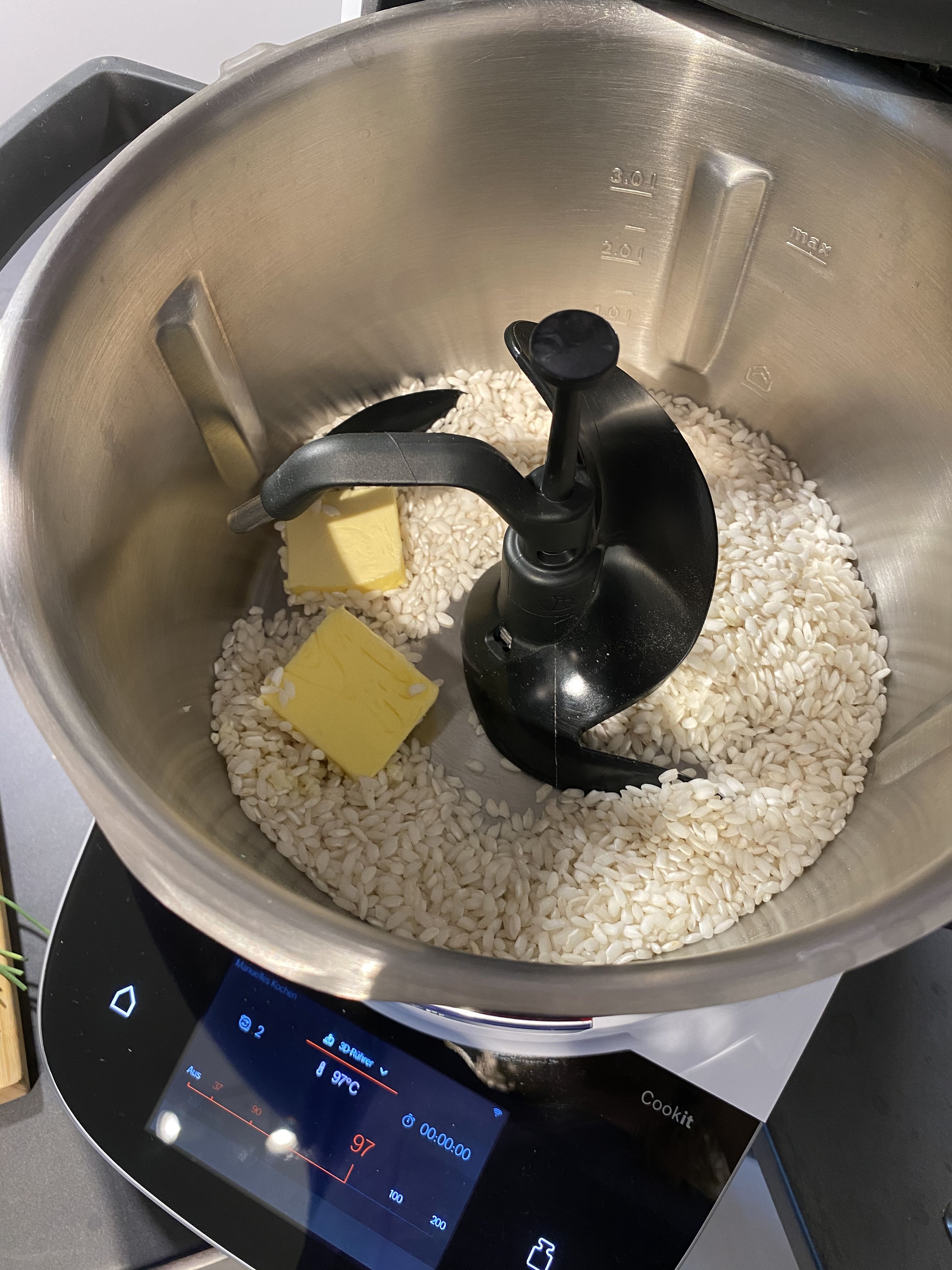 Das Cookit-Universalmesser in den Cookit einsetzten. 
Den Knoblauch und die Zwiebeln schälen, halbieren und in den Topf geben, den Deckel verschließen und zerkleinern (Universalmesser l Stufe 14 l 8 Sek.).
Anschließend das Universalmesser entfernen, den 3D-Rührer einsetzen, die Butter und den Risottoreis zufügen und alles anbraten (3D-Rührer l Stufe 3 l 110°C l 10 Min.).