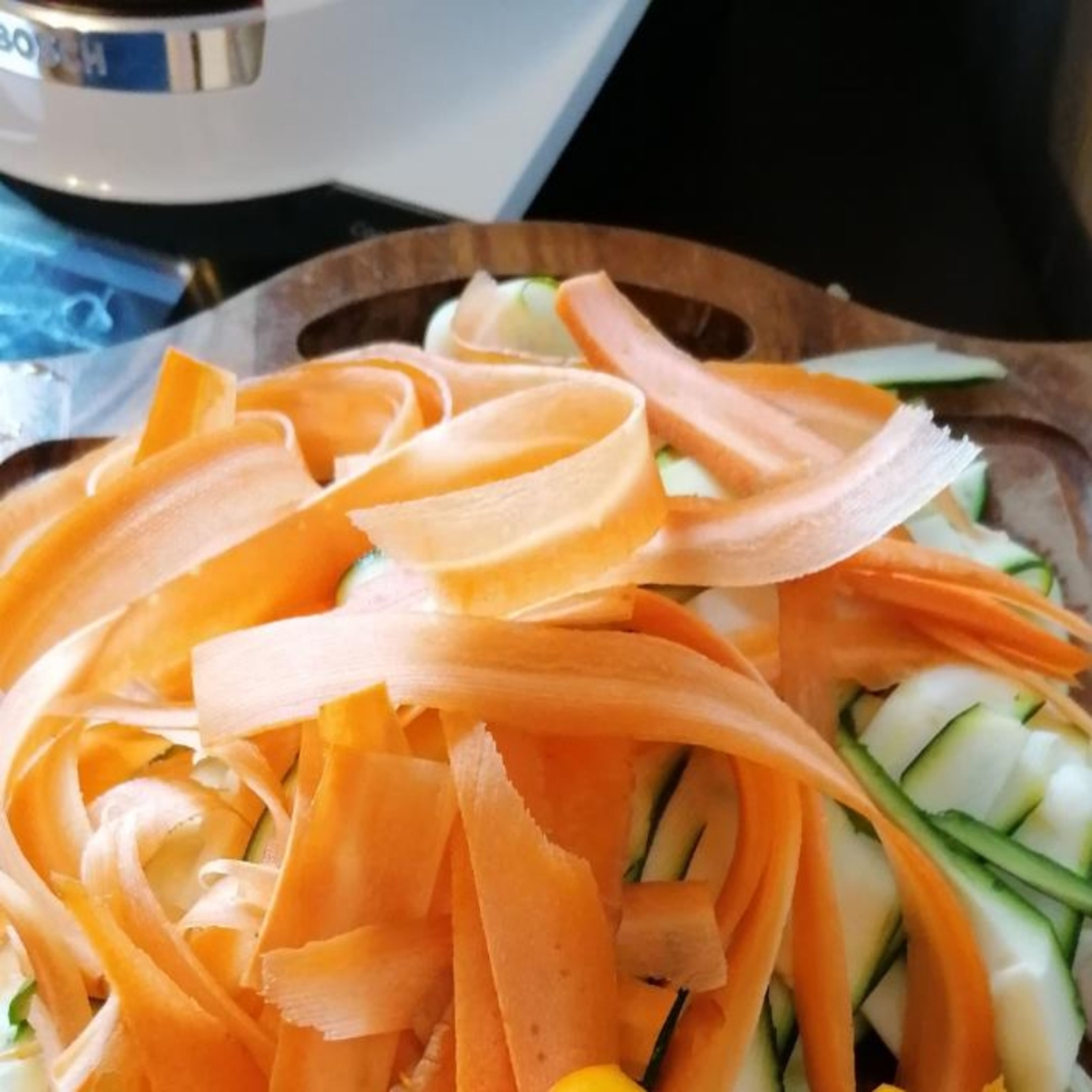 In der Zwischenzeit die Zucchini und Karotte vierteln und mit einem Hobel in dünne Streifen hobeln oder mit einem Messer in feine Streifen schneiden.