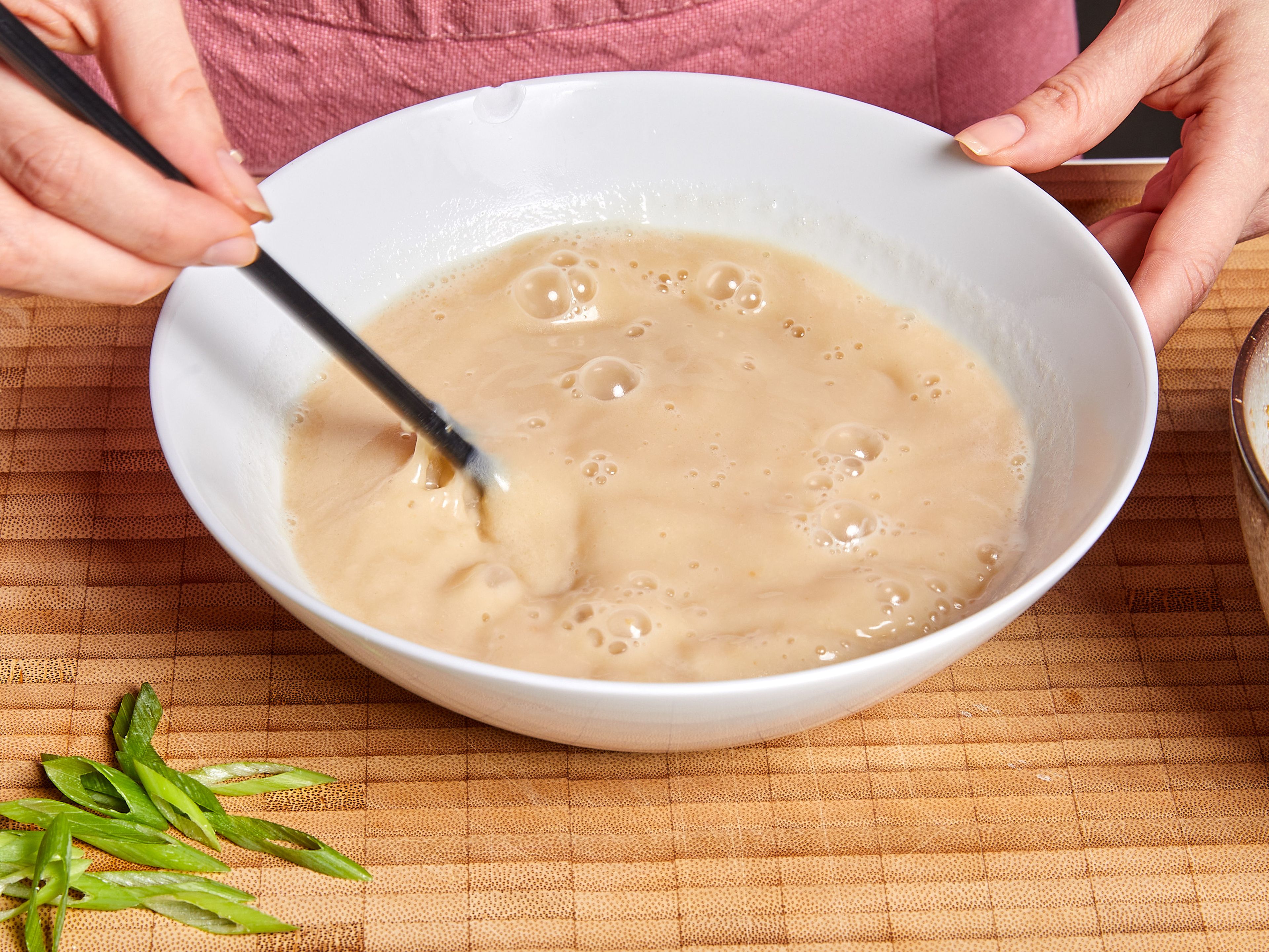 In dem zuvor verwendeten Topf Gemüsebrühe und Sojamilch bei mittlerer Hitze zum Kochen bringen. Die Suppenbasis auf Schüsseln verteilen, die heiße Brühe darüber gießen und mit Stäbchen verrühren, bis alles vermischt ist. Ramen-Nudeln, Pak Choi, Mais und Sojahack auf die Schüsseln verteilen. Mit Frühlingszwiebelgrün, Sesam und Chiliöl garniert servieren.