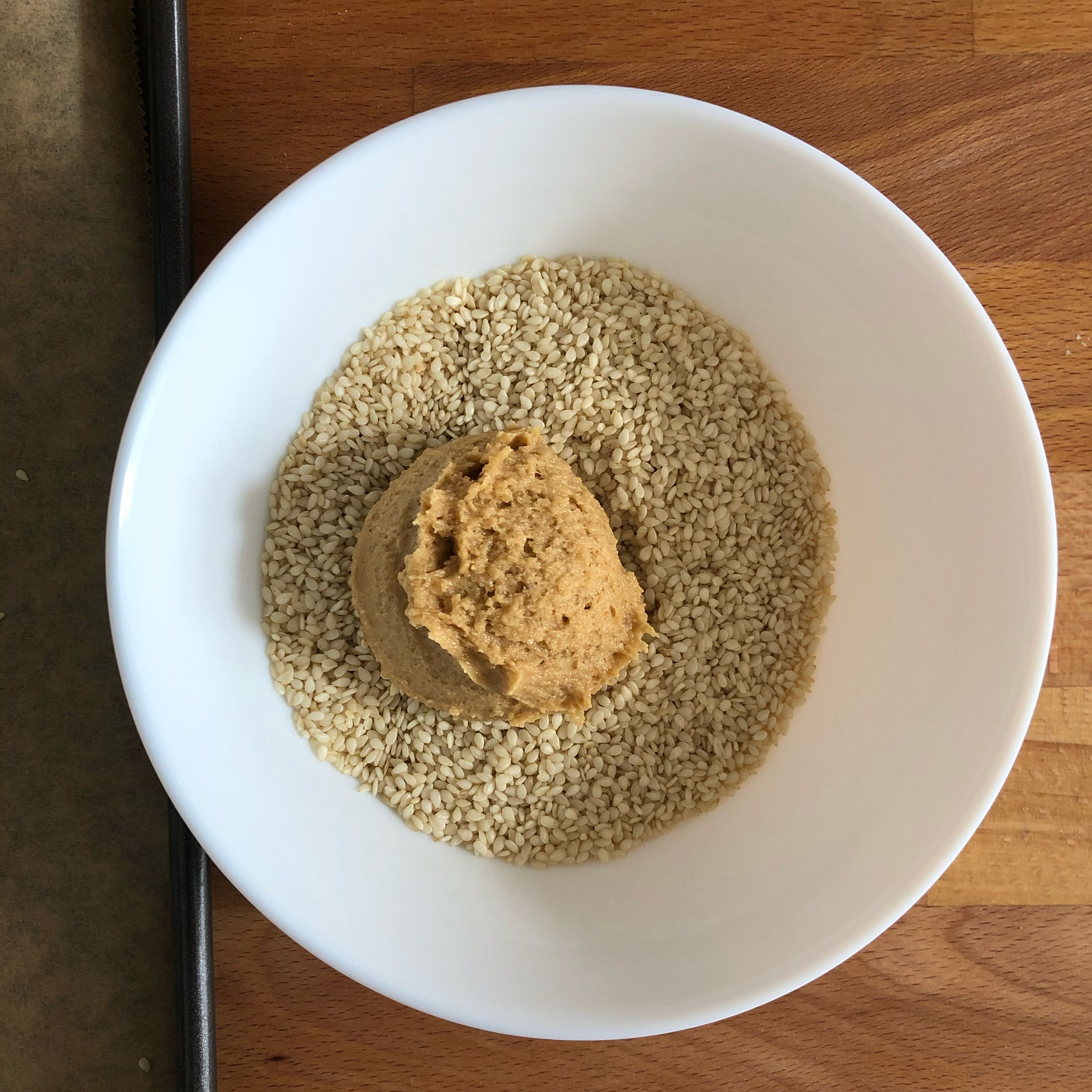 Add sesame seeds to a bowl. Use an ice cream scooper to scoop some of the cookie dough, then add to the bowl of sesame seeds and cover the ball. Transfer to a parchment-lined baking sheet. Repeat until all the cookie dough is gone, then cover the baking sheet with plastic wrap and chill dough for at least 2 hours, or overnight.