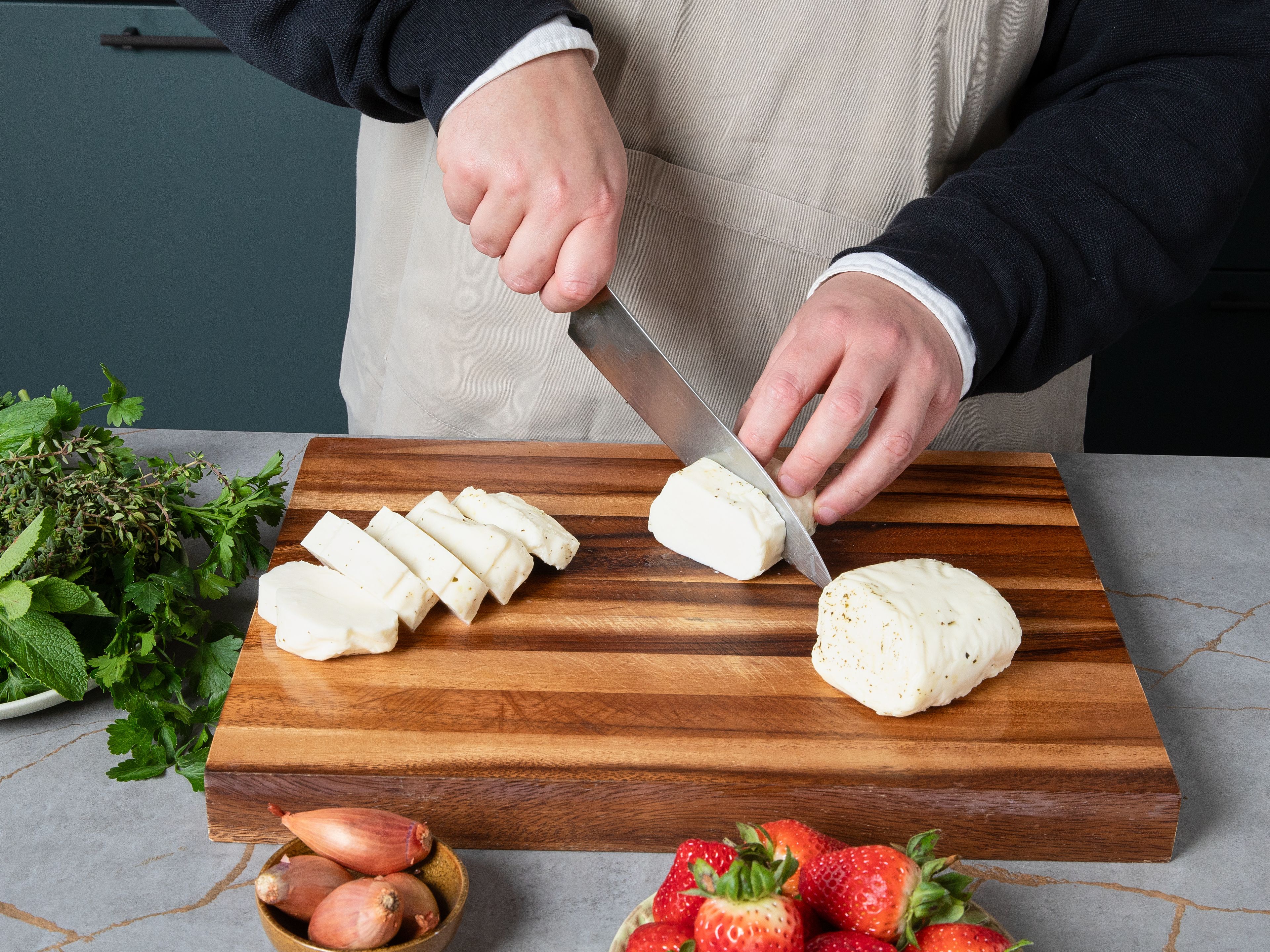 Den Halloumi in ca. 1,5 cm dicke Scheiben schneiden. Erdbeeren und Schalotten fein würfeln. Den Knoblauch fein hacken. Anschließend die Blätter von Minze, Petersilie und Thymian von den Stielen zupfen und die Blätter fein hacken.