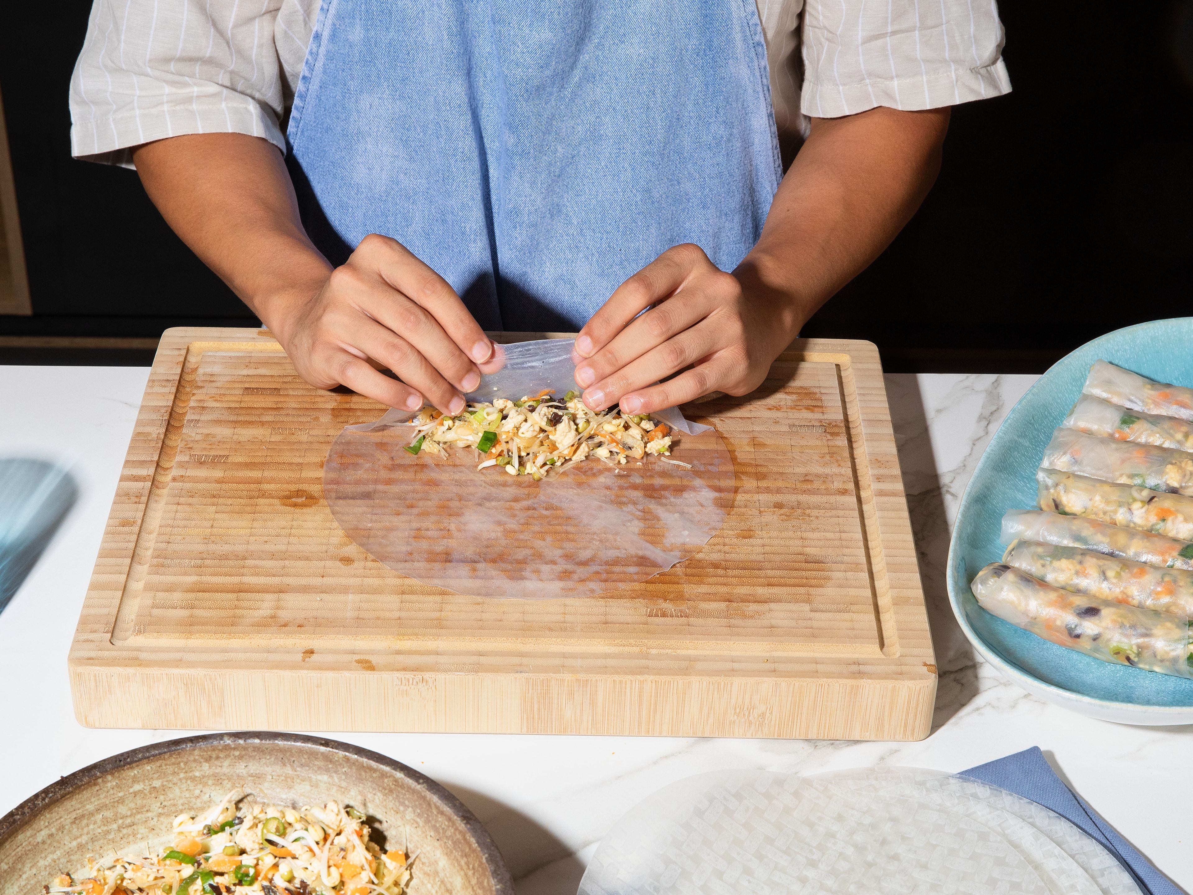 Dampen rice paper in water until flexible. Place filling centrally on the bottom third, fold in side edges, and roll tightly and sealed to prevent any leaking during frying.