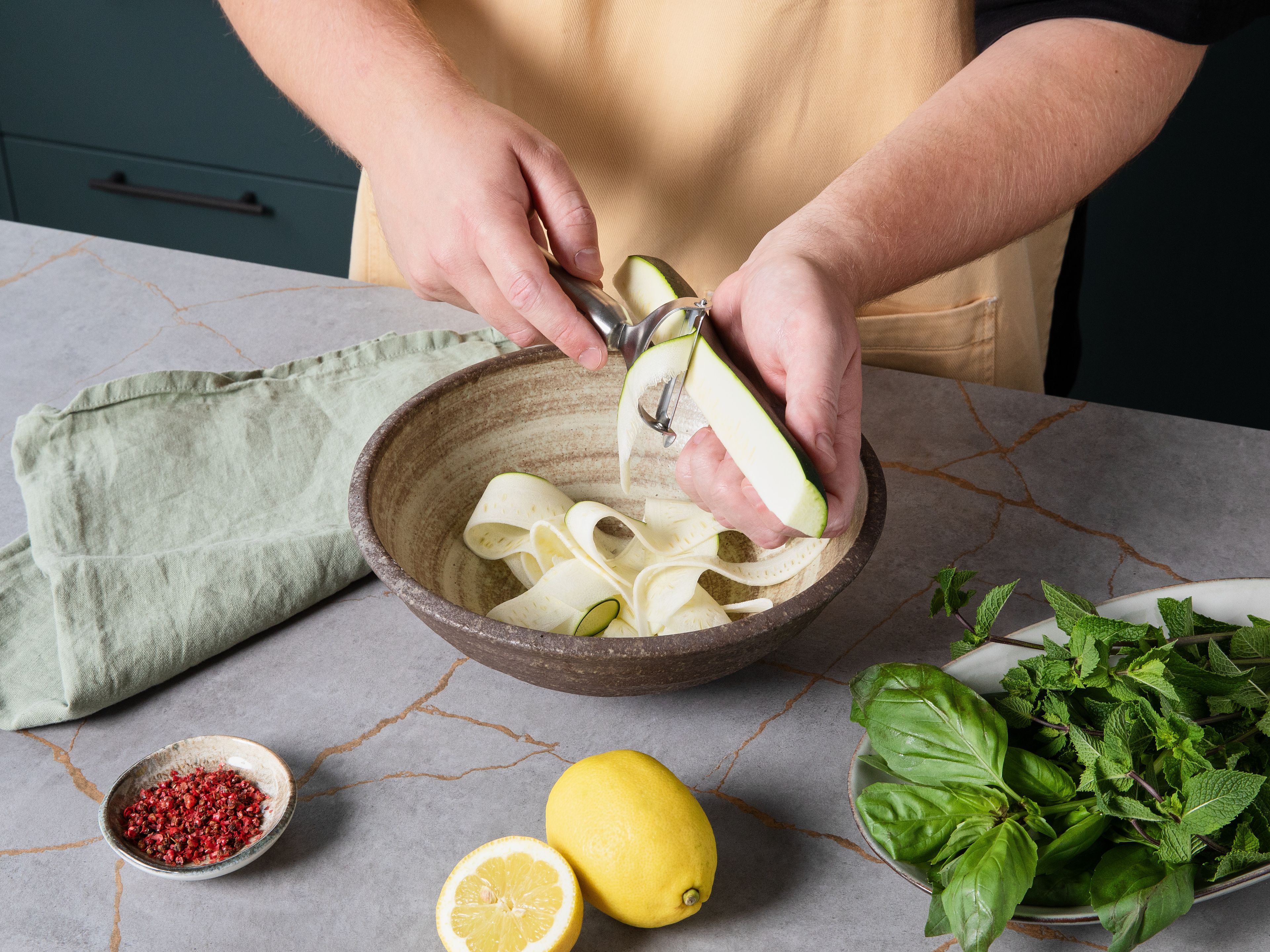 Die Zucchini der Länge nach halbieren. Mit einem Gemüsehobel oder einem Sparschäler in feine Scheiben schneiden. Die Zucchinistreifen mit Basilikum, Minze, Olivenöl und Zitronensaft  in eine Schüssel geben. Mit einer Prise Salz und etwas rosa Pfeffer würzen und beiseite Stellen.