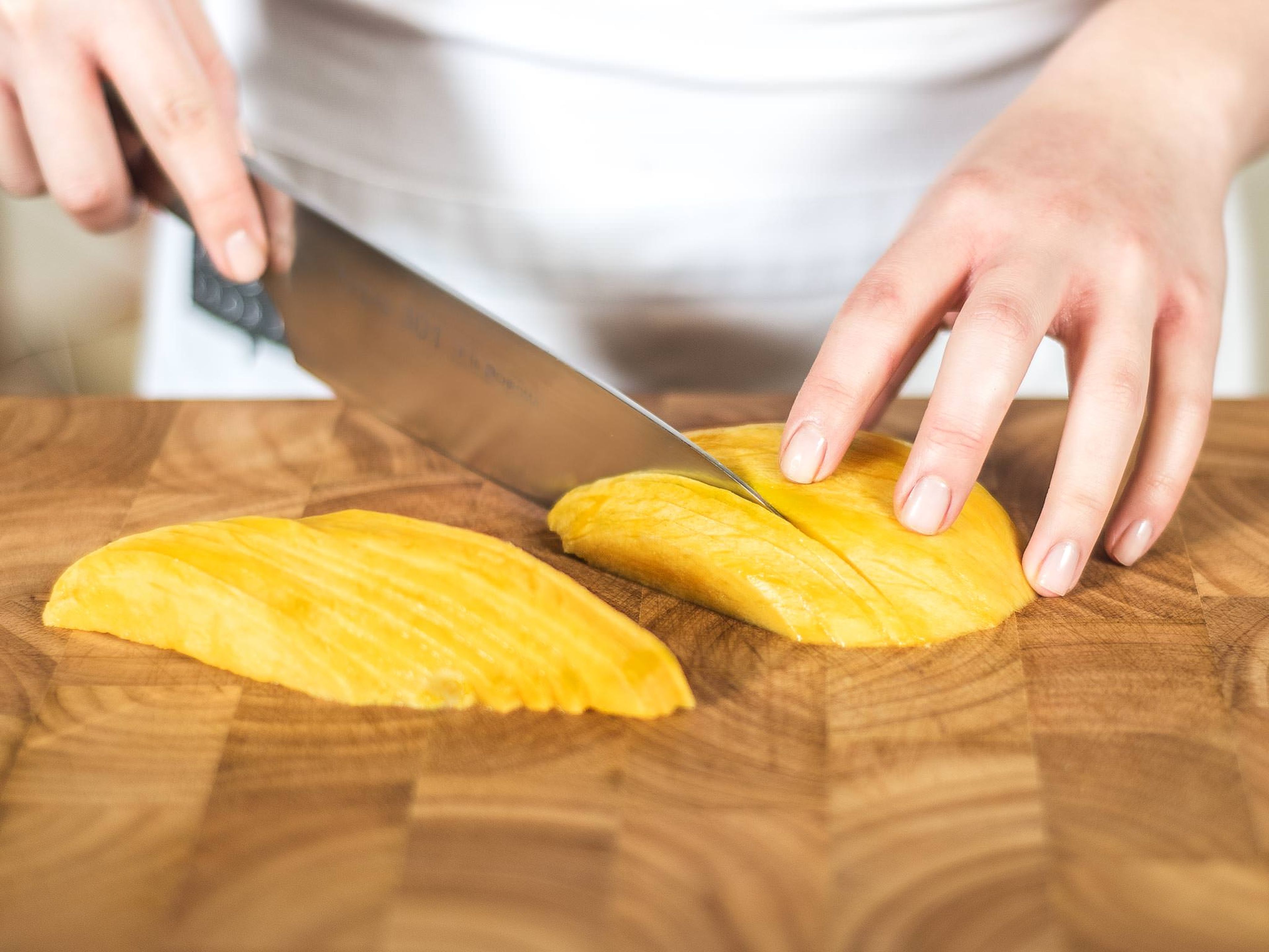 Now, peel the mango and carefully cut the flesh from the stone. Next, slice the two large sides of the fruit into fine strips.