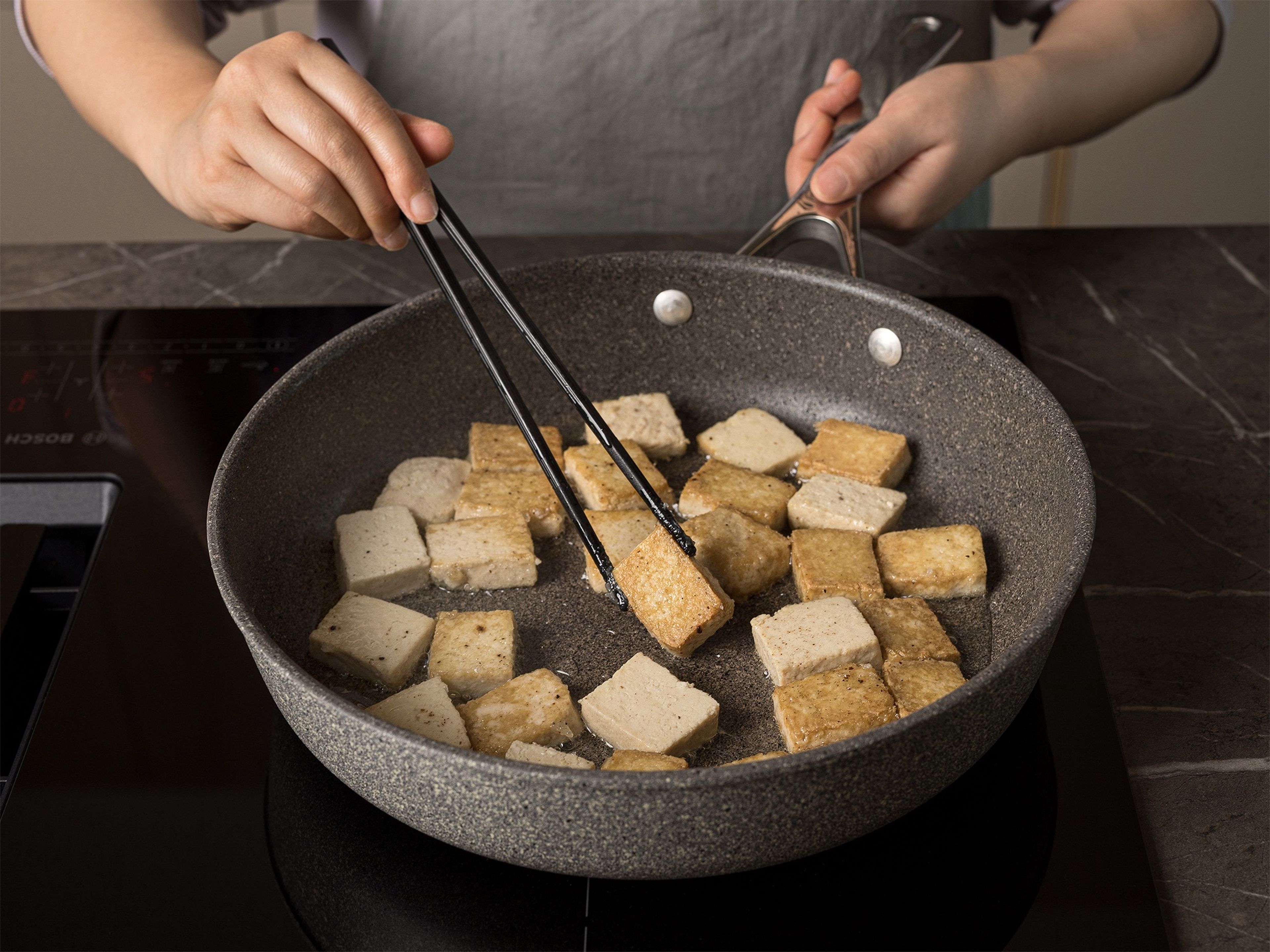 In einer großen beschichteten Pfanne Öl bei mittlerer bis hoher Temperatur erhitzen. Die Tofuwürfel in einer Schicht hineingeben und braten, bis die Unterseite goldbraun ist, dann wenden und auf der anderen Seite braten (ca. 5 Min. pro Seite). Herausnehmen und beiseitestellen. In der gleichen Pfanne die Soße zugeben und ca. 3-5 Min. köcheln lassen, bis sie eindickt. Die Hälfte der Soße für die Nudeln aufheben. Die Tofuwürfel in die restliche Soße geben und vermengen, bis der Tofu mit der Glasur überzogen ist.