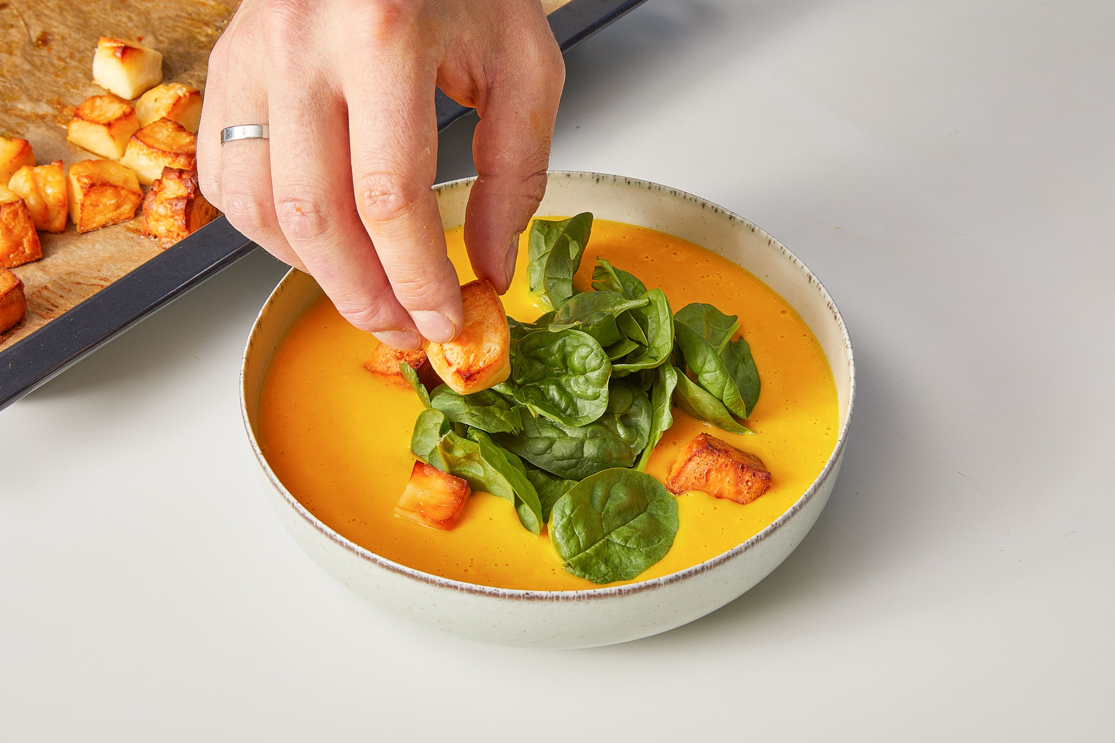 Once the soup has reached the desired consistency, pour into serving bowls. Place a handful of baby spinach in the center of each and top with the halloumi pieces from the oven. Garnish with chili flakes, pepper, lemon zest and a drizzle of olive oil. Serve with bread, if desired.